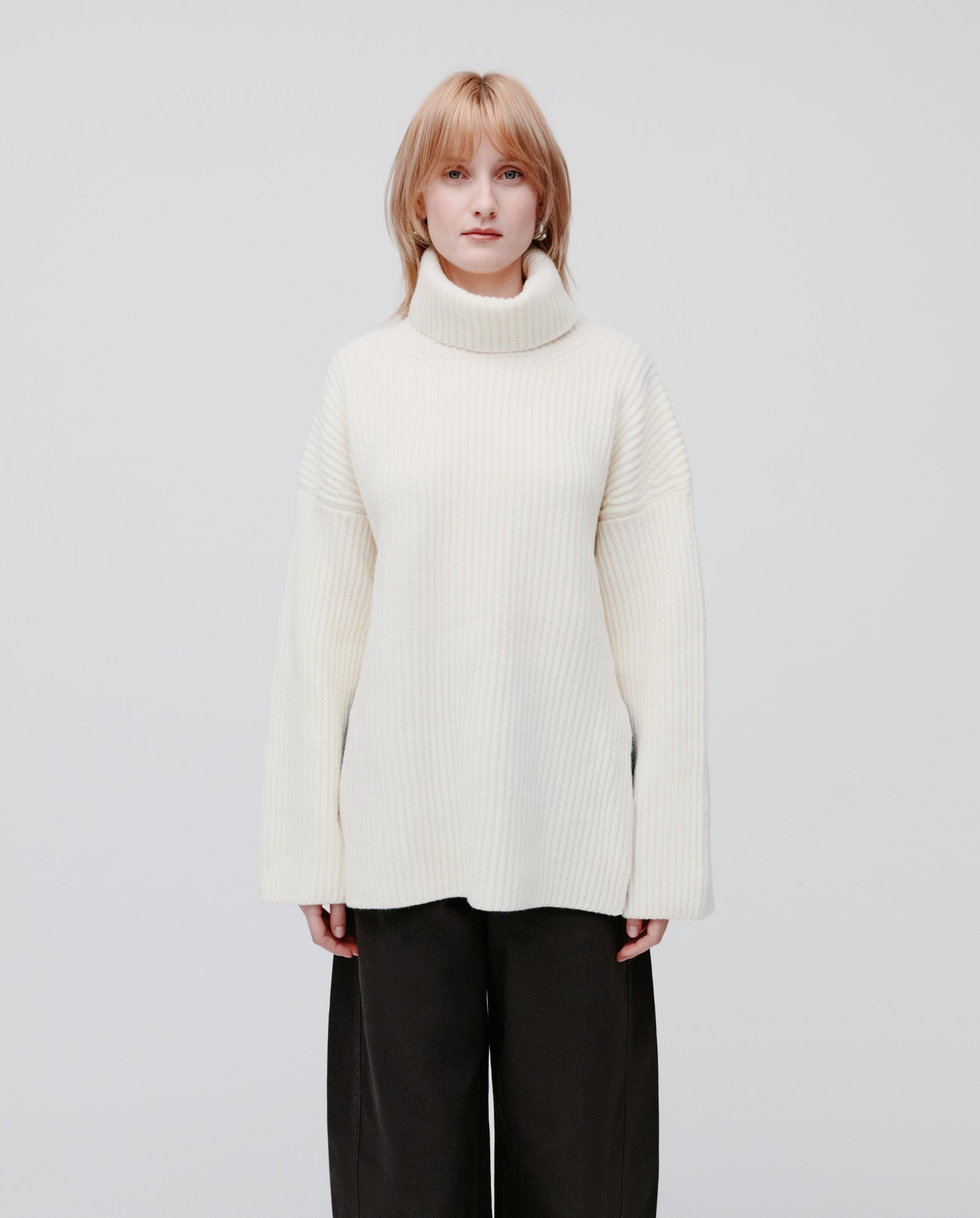 Model wears the IVY OAK KYOMI ANN cream high neck jumper with black pants, standing against a plain light background.