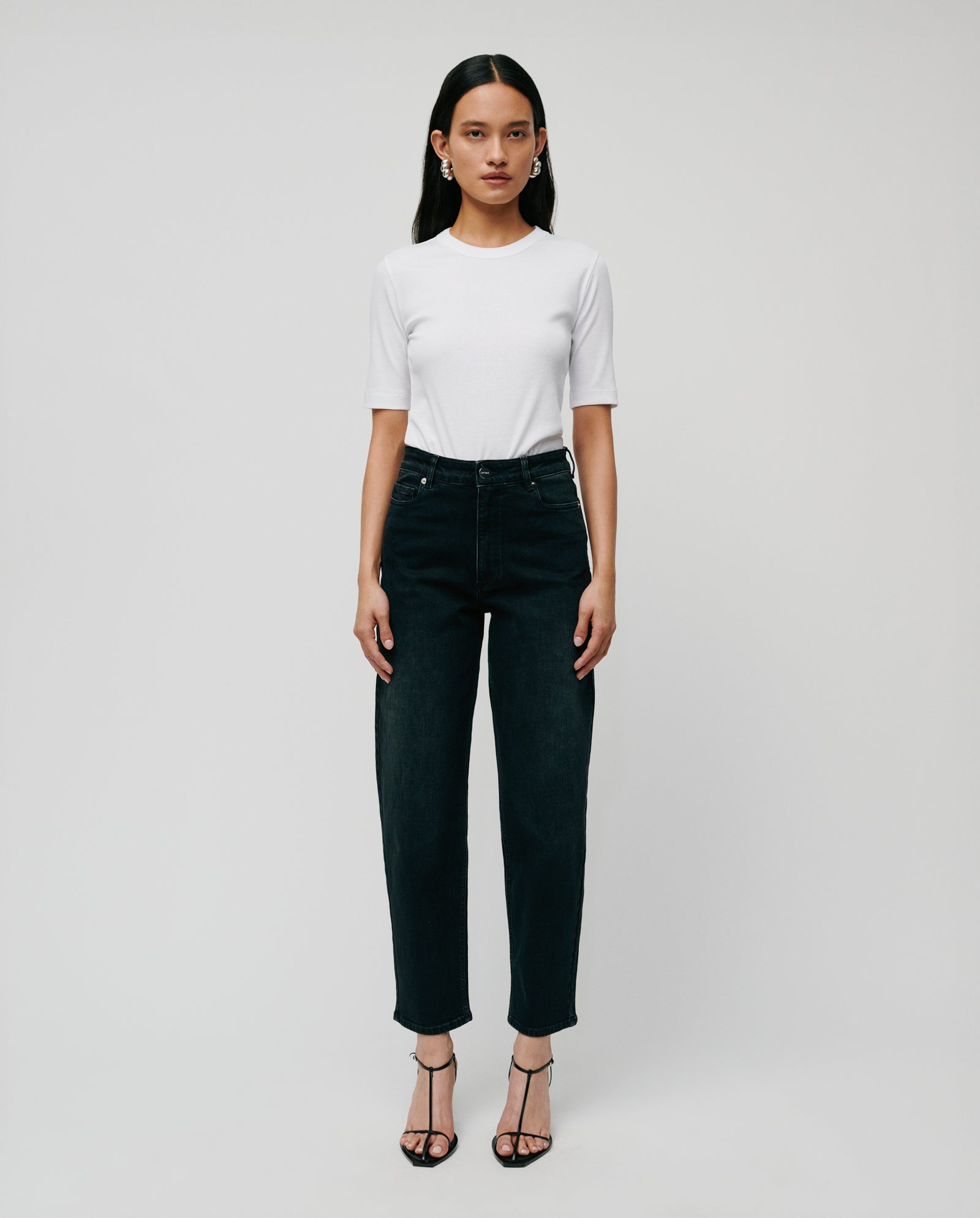 A woman stands against a plain background wearing a white short-sleeve shirt, IVY OAK PETRA Trousers with patched pockets, and black heels.