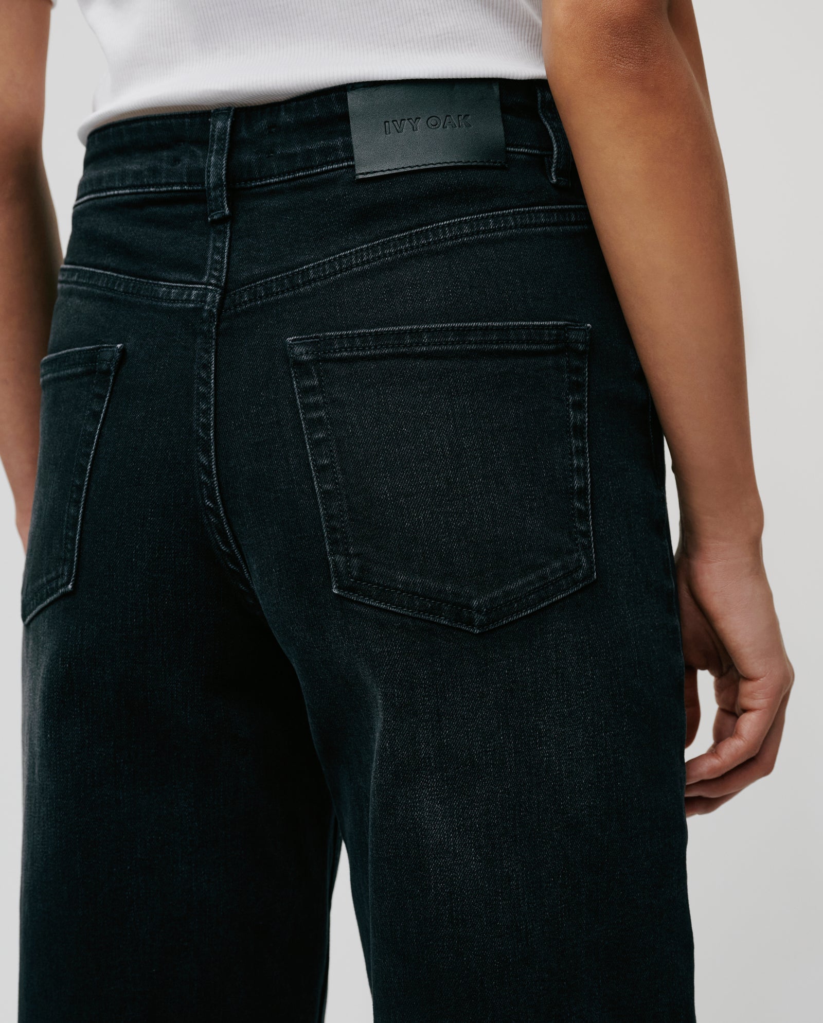 Model wearing black IVY OAK PETRA Trousers and a white top, shown from the back to highlight the patched pocket detail and signature barrel leg silhouette.