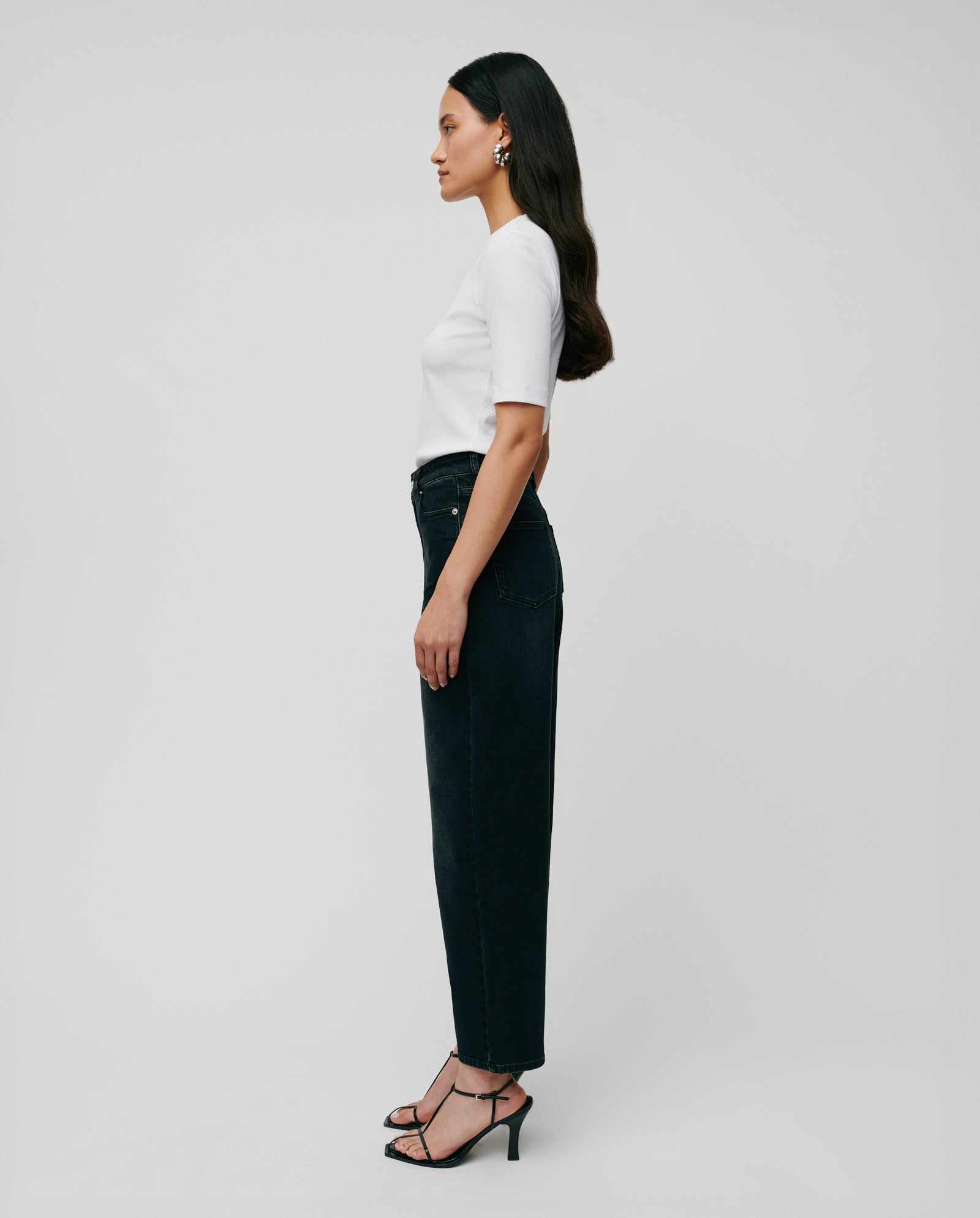 A woman in a white top wears IVY OAKs PETRA Trousers, featuring patched pockets and a barrel leg silhouette, posed in profile against a plain white background.