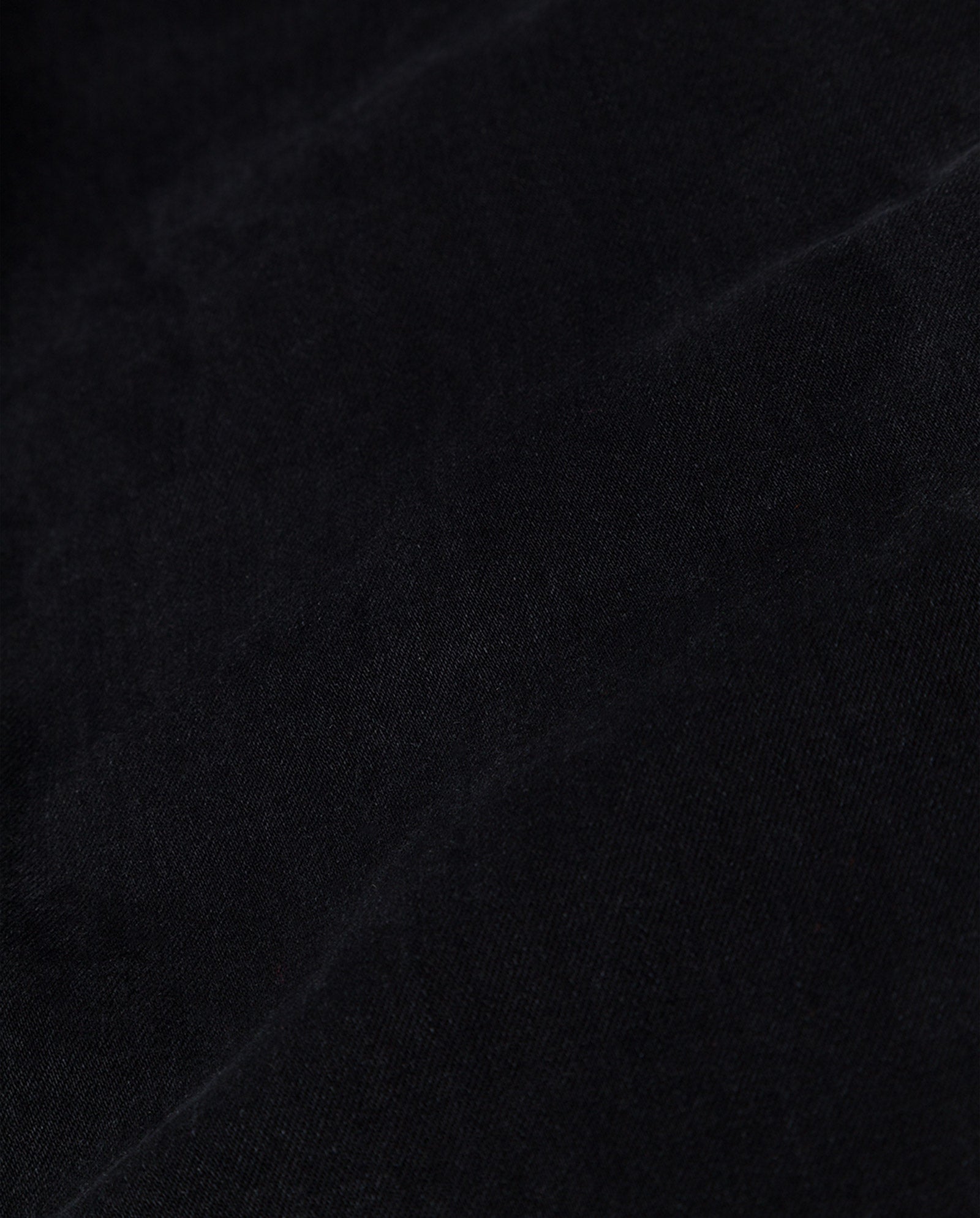 Close-up of black fabric texture with visible creases and subtle light reflections, capturing the signature style of IVY OAKs PETRA Trousers.