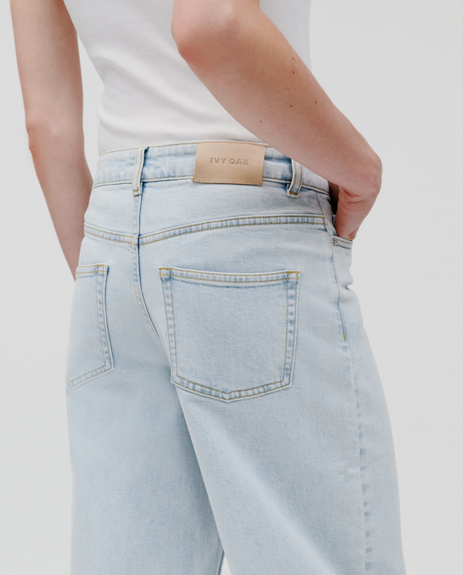A person wearing PETRA Trousers by IVY OAK—light blue barrel leg jeans with patched pockets and a white top; the jeans feature a beige IVY OAK label on the waistband.