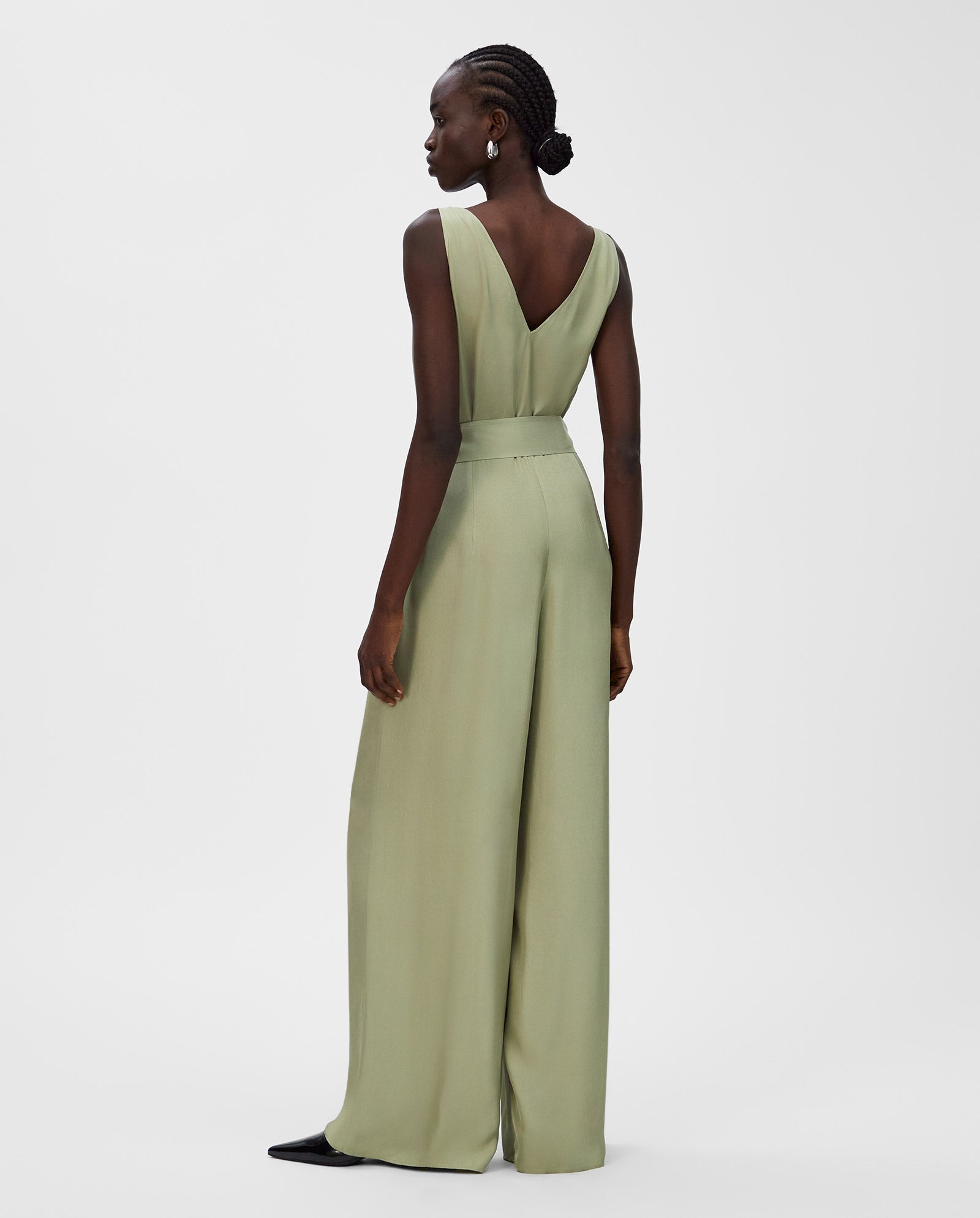 Woman in a light green IVY OAK PATRICIA Jumpsuit crafted from soft Naia acetate, with wide legs and sleeveless design, shown from the back against a white background.