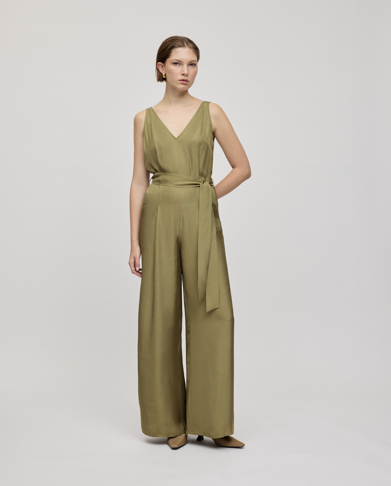 A woman wears the IVY OAK PATRICIA Jumpsuit in olive green, made from Naia acetate with wide legs and an adjustable belt, standing against a plain background.