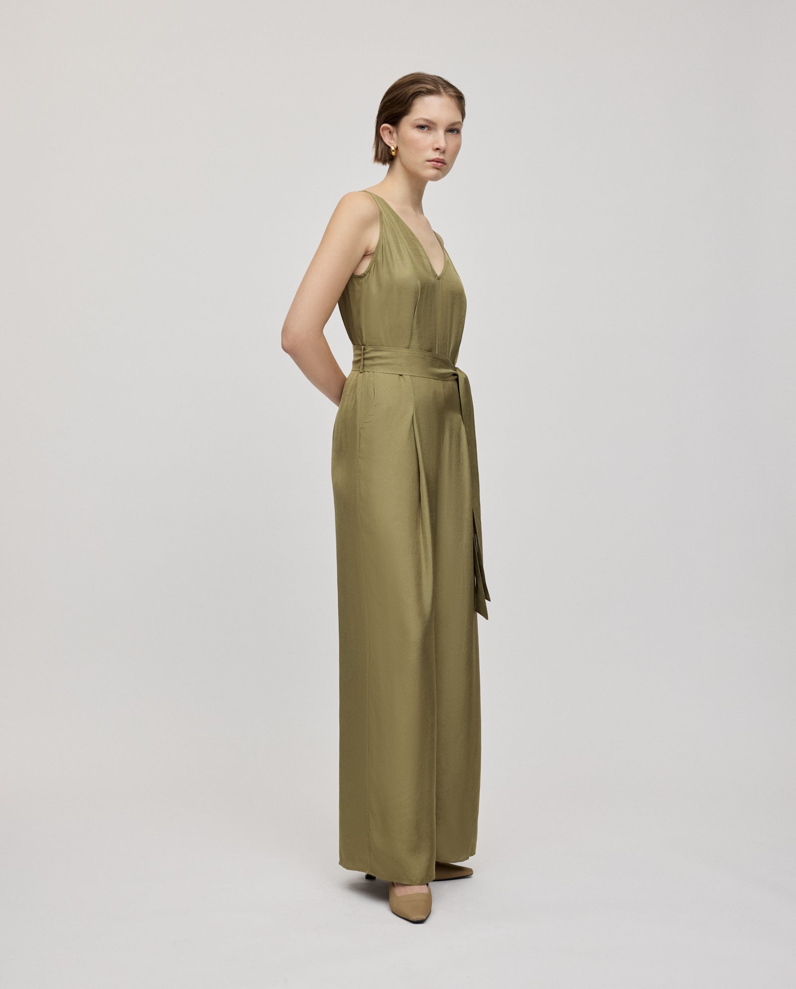 A woman wears the IVY OAK PATRICIA Jumpsuit in sleeveless olive green Naia acetate, with wide legs and an adjustable belt, standing against a plain background.