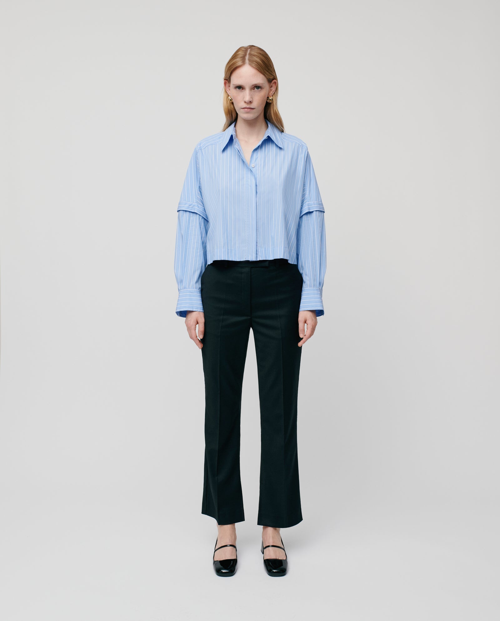 A woman stands against a white background wearing a blue shirt, IVY OAK POLINA Trouser, black shoes, and a JOLANKA blazer.