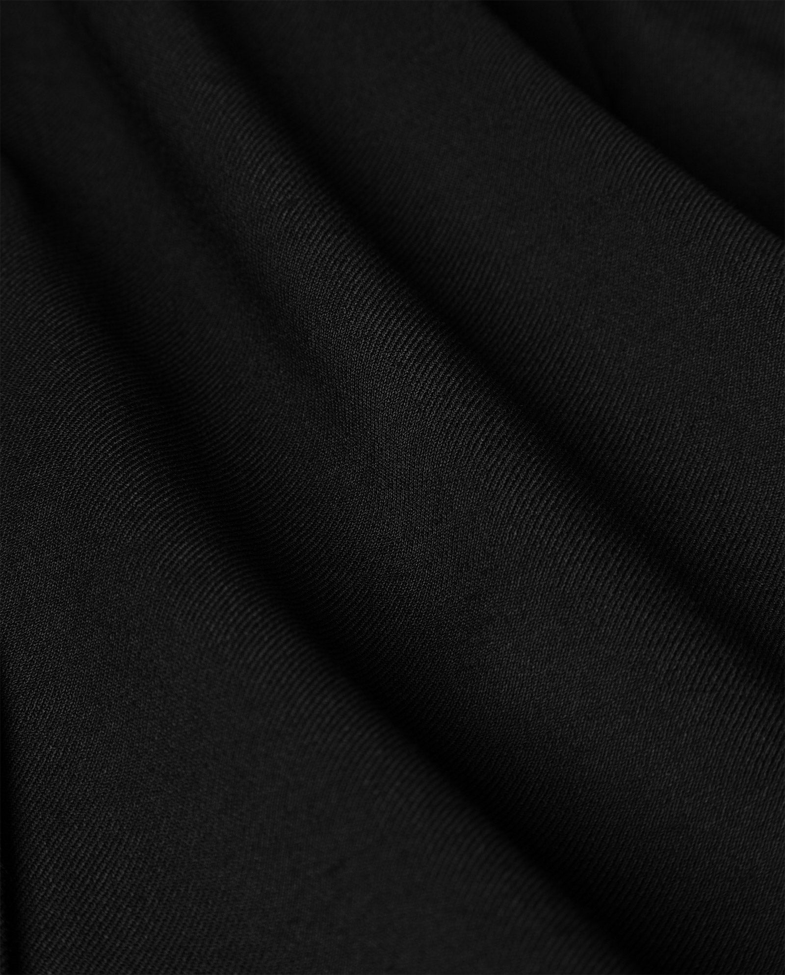 Close-up of smooth black fabric with soft folds and diagonal weave texture, featured on the fitted and flared POLINA Trouser by IVY OAK.