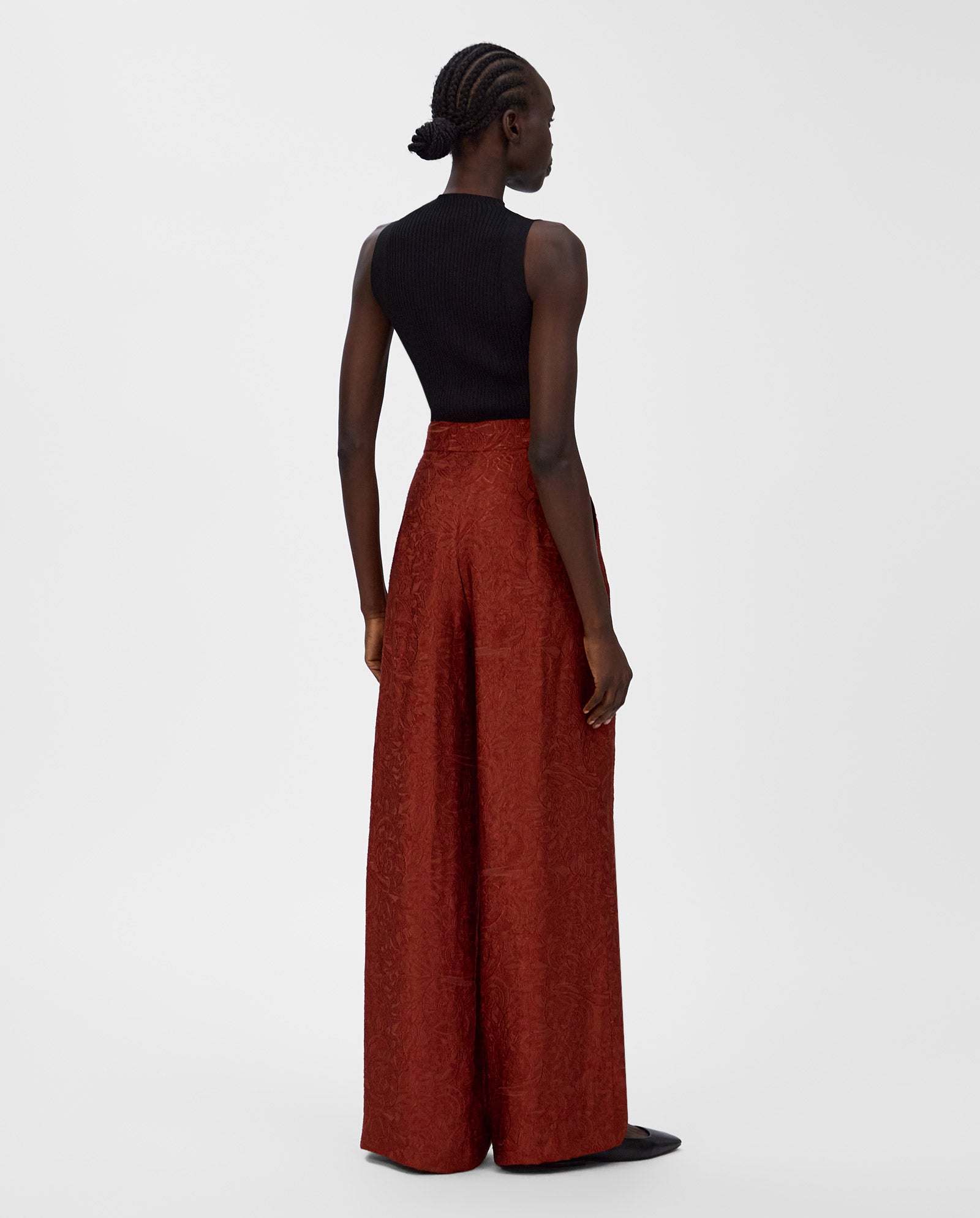 A woman faces away, wearing a black sleeveless top and high-waisted, wide-leg red fil coupé PRIYA Trouser by IVY OAK.