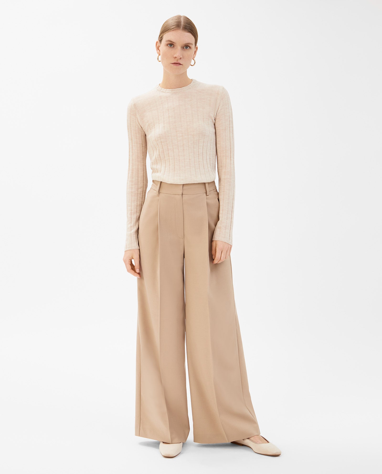 A woman wears the IVY OAK PRESCILLIA Trouser—tan wide-leg style—with a beige long-sleeve top and matching flats against a white background. Pair with a coordinating blazer for an effortlessly sophisticated look.