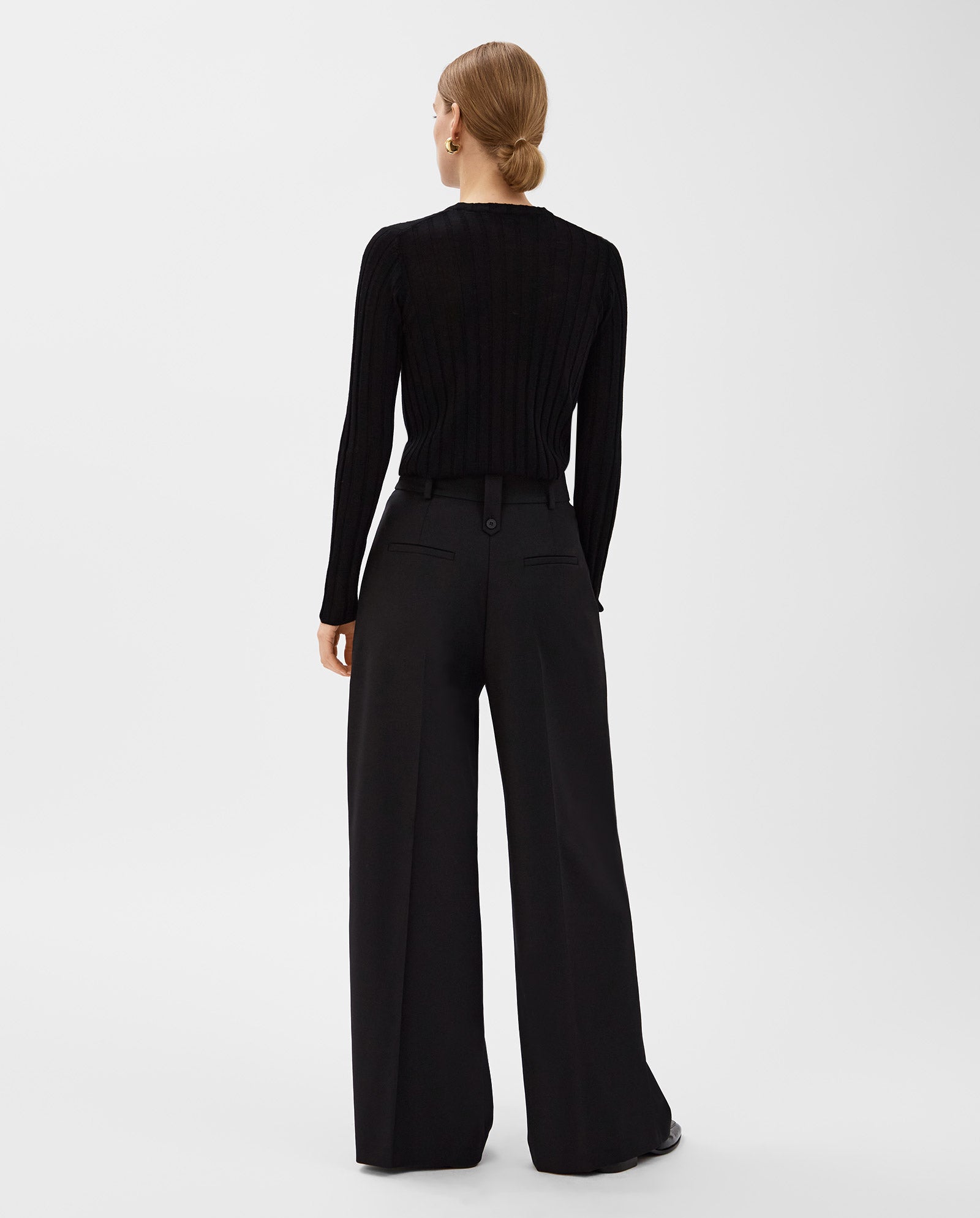 A woman stands facing away against a plain background, wearing a black long-sleeve top and IVY OAKs PRESCILLIA Trouser, wide-leg style designed for taller frames.