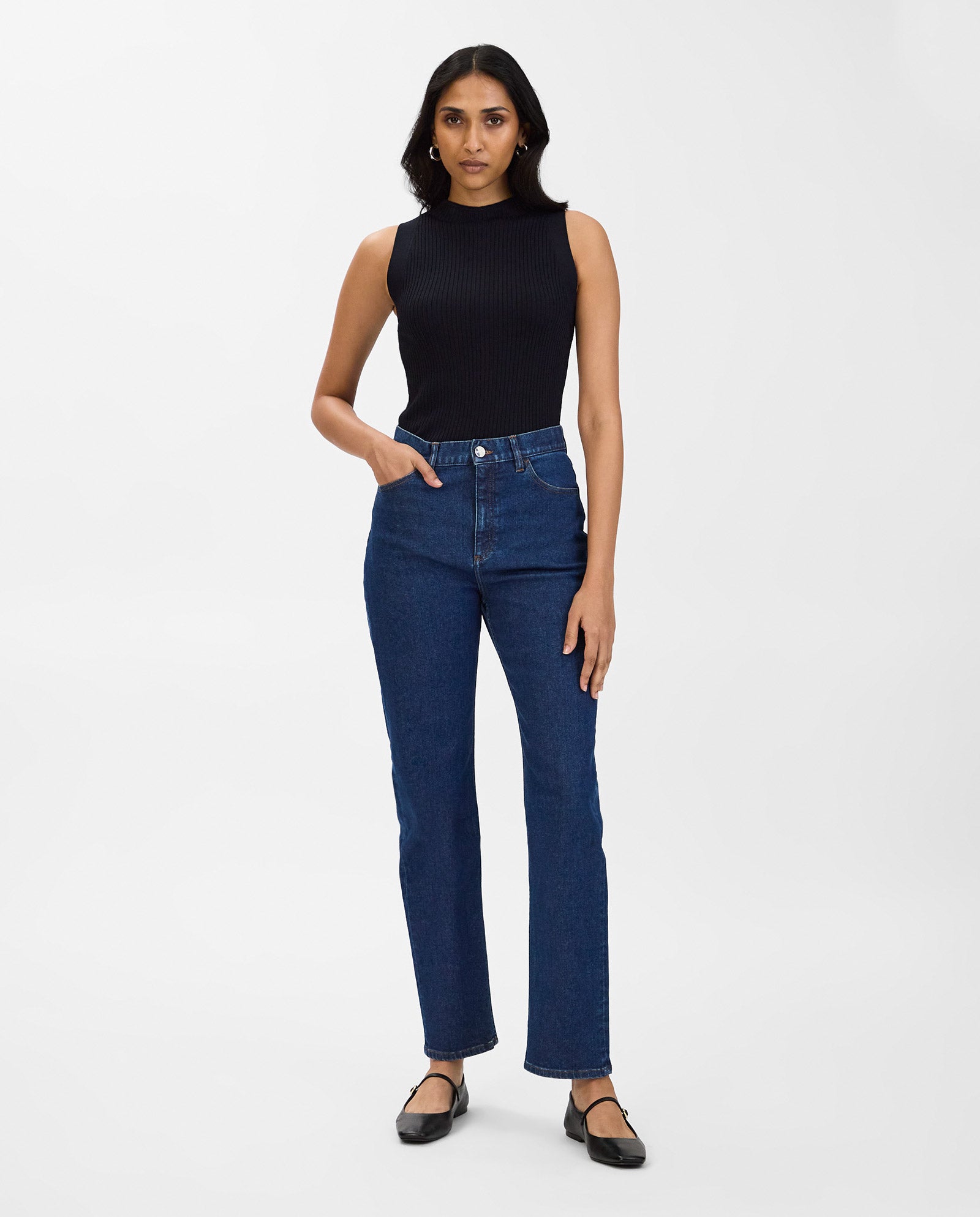 A woman in a black sleeveless top, IVY OAK POEMA Trousers with straight legs and contrast stitching, and black flats stands against a plain white background.