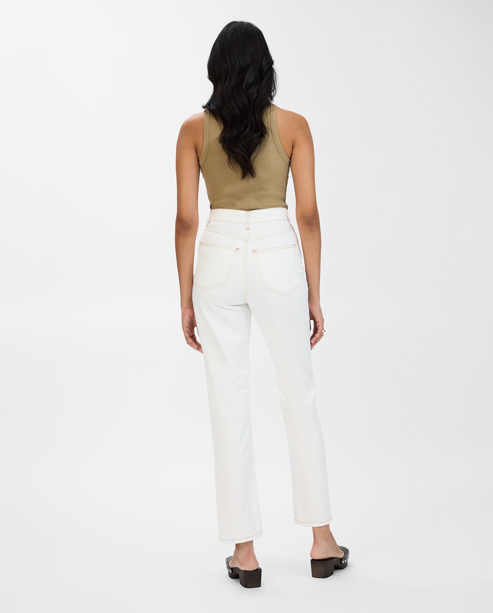 A woman stands facing away, wearing a tan sleeveless top, straight leg white POEMA Trousers by IVY OAK, and black sandals against a white background.