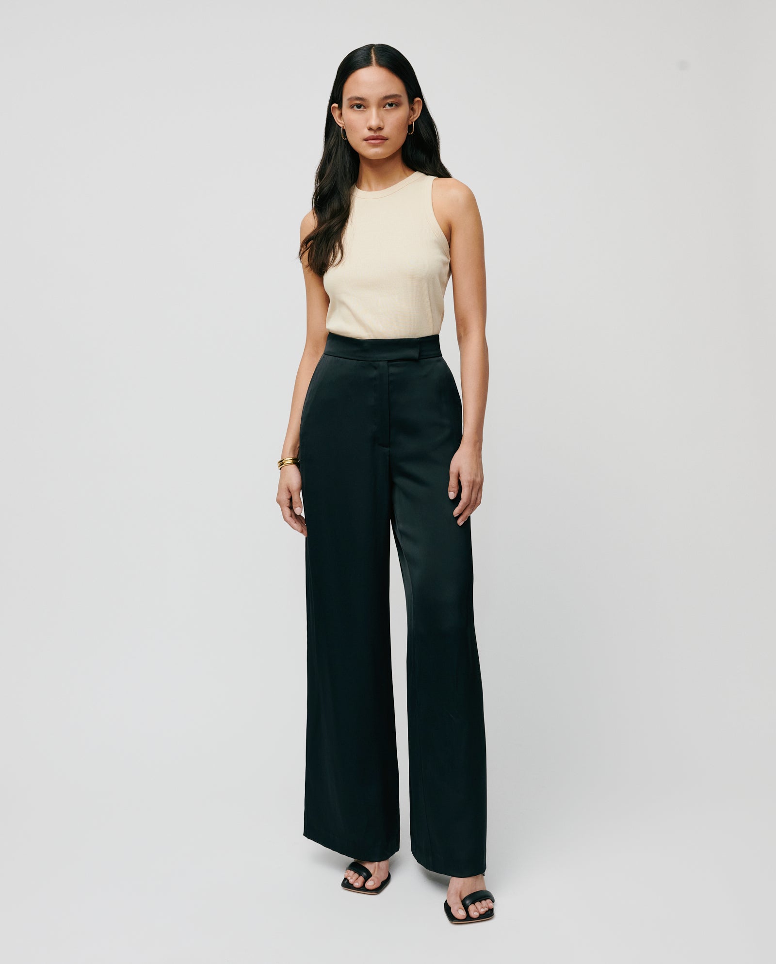 Woman wearing a sleeveless beige top, high-waisted IVY OAK PRIYA ANN Trouser, and black sandals, standing against a plain background.
