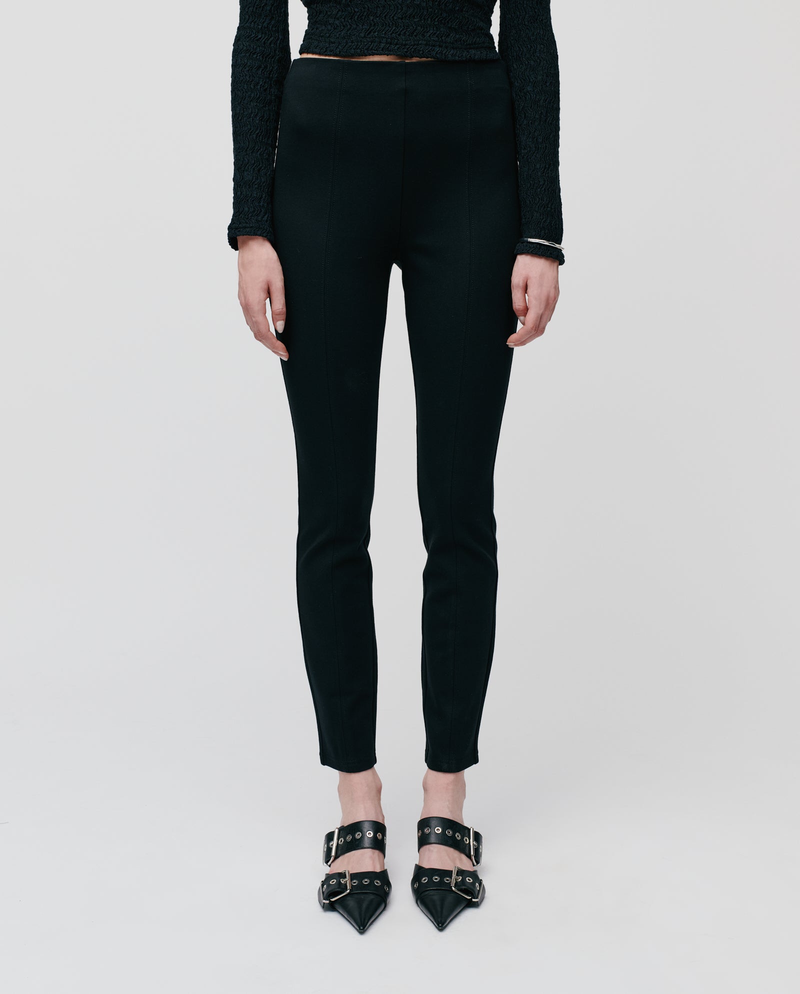 A woman wears IVY OAKs PHILIPPA EVE Trousers with stitched seams, styled with a black textured top and pointed buckle shoes, creating an elegant silhouette against a white background.