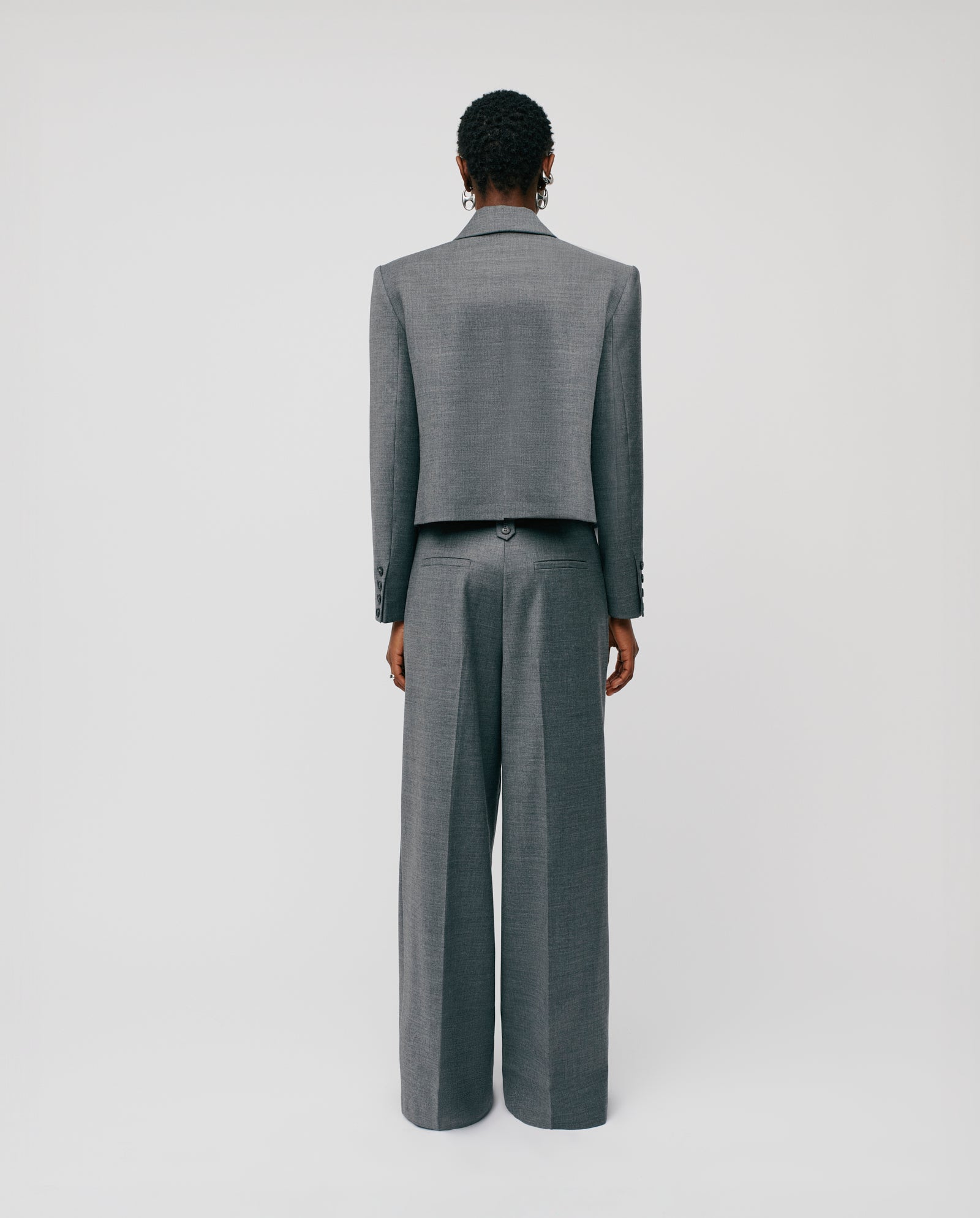 A person with their back to the camera models IVY OAK’s PRESCILLIA wide-leg trousers and a JOLANKA blazer, standing against a plain background.