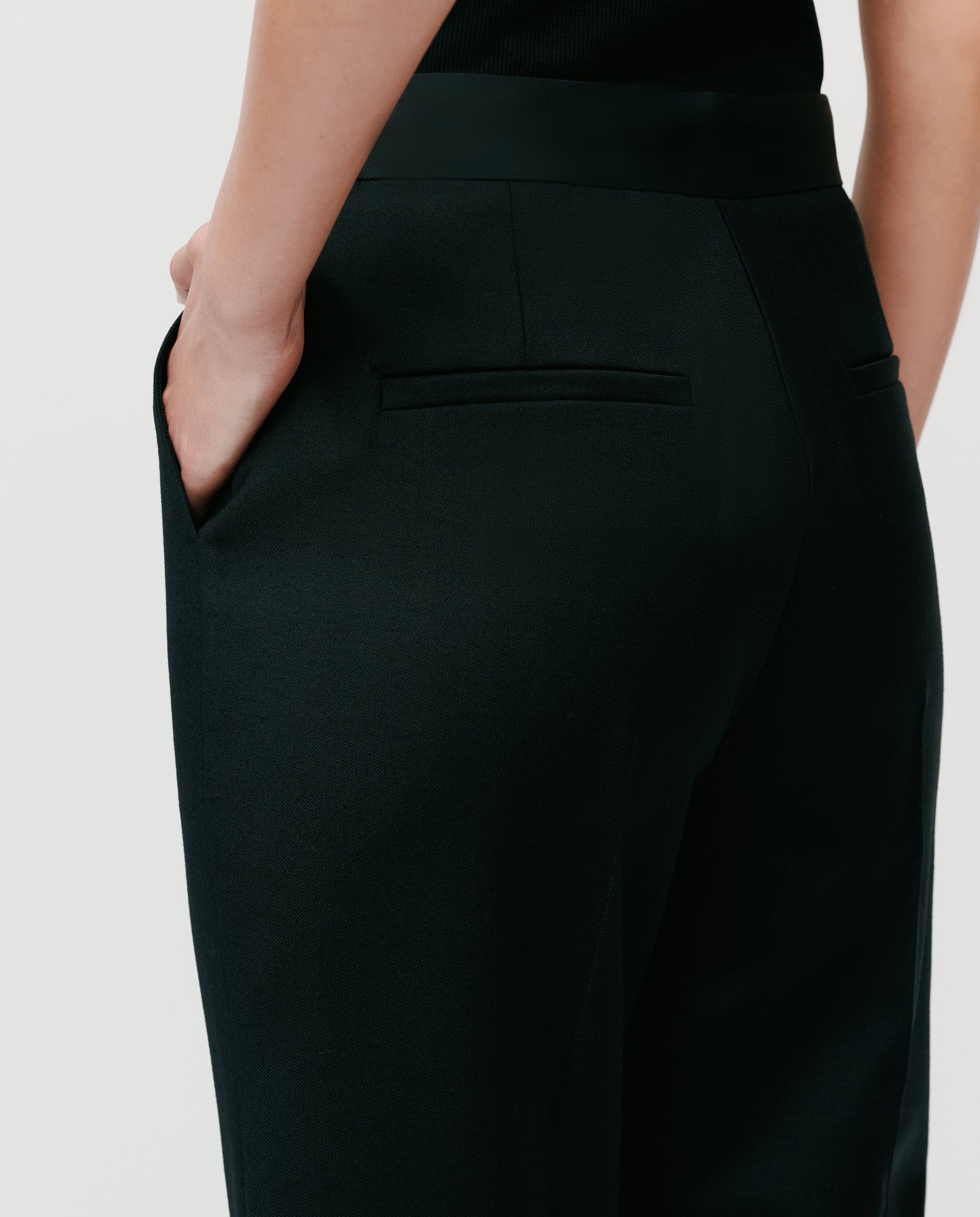 A person wearing IVY OAK POLINA ROSE trousers with a shiny waistband, one hand in their pocket, shown from the back and side.