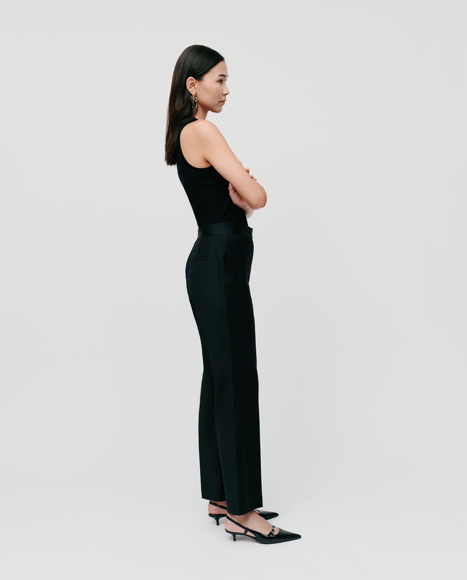 Woman wearing IVY OAKs POLINA ROSE Trousers, standing sideways with arms crossed against a white background.