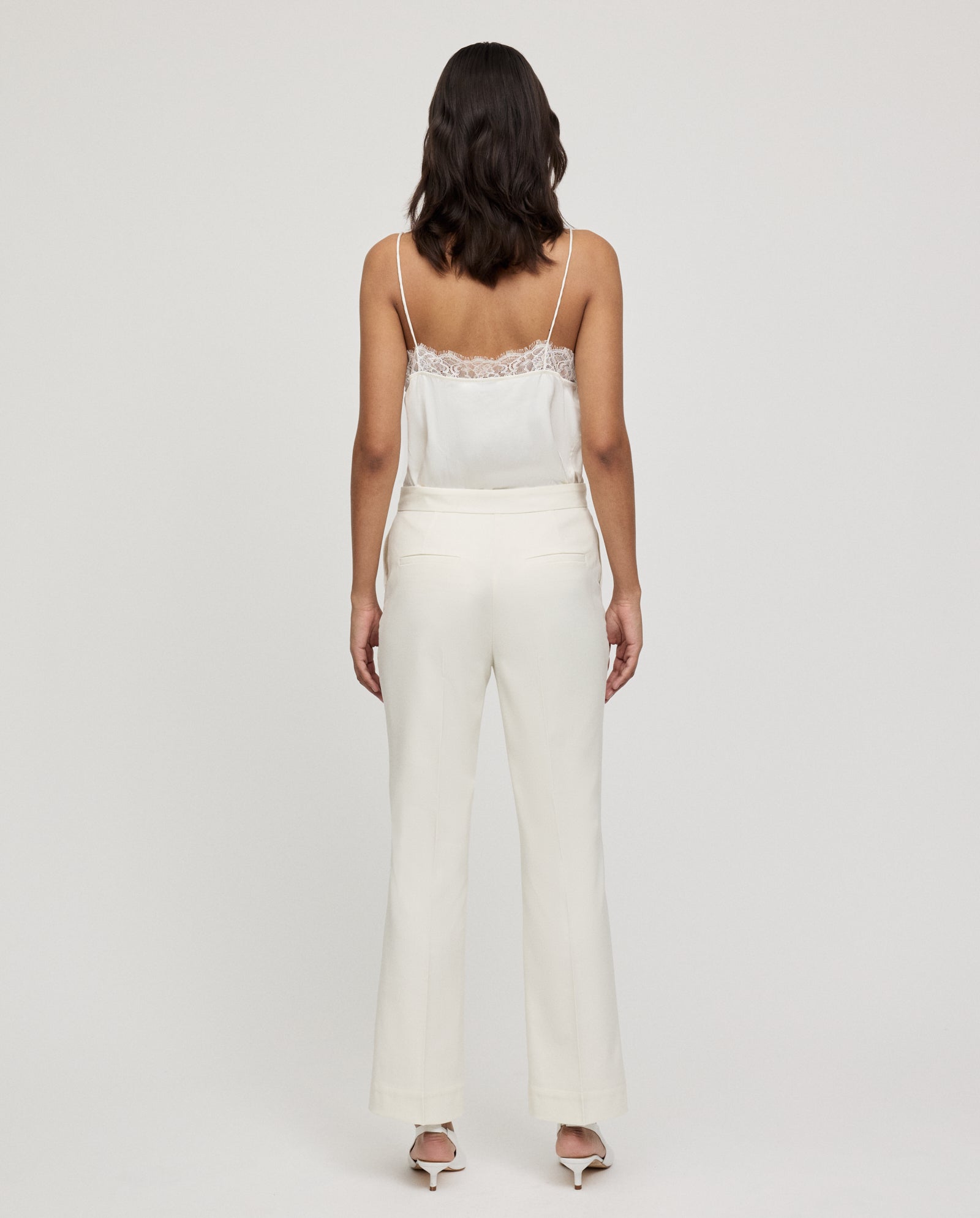 Woman in a white lace-trim camisole and IVY OAK POLINA ROSE Trousers stands facing away against a plain background.