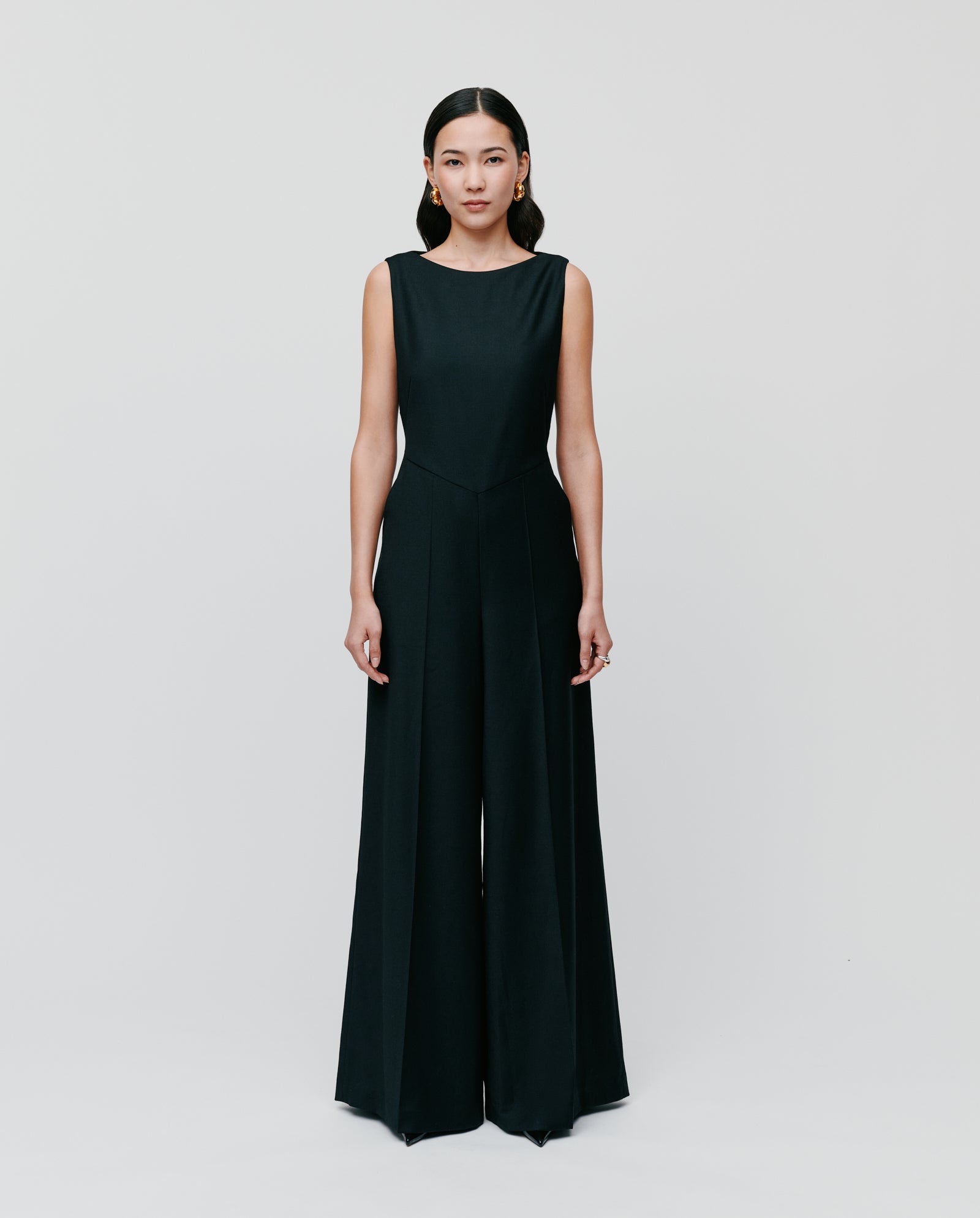 A woman wears the IVY OAK PEPPINA Jumpsuit, featuring a sleeveless design, boat neckline, and wide legs, standing against a plain white background.