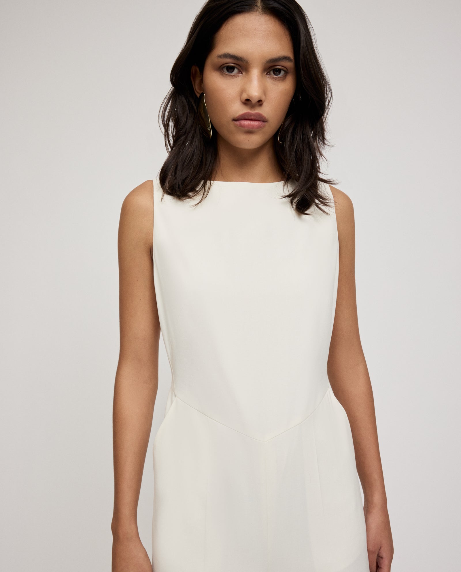 Woman with dark hair wears the IVY OAK PEPPINA Jumpsuit, featuring a cream hue, boat neckline, and wide legs, standing against a plain background.