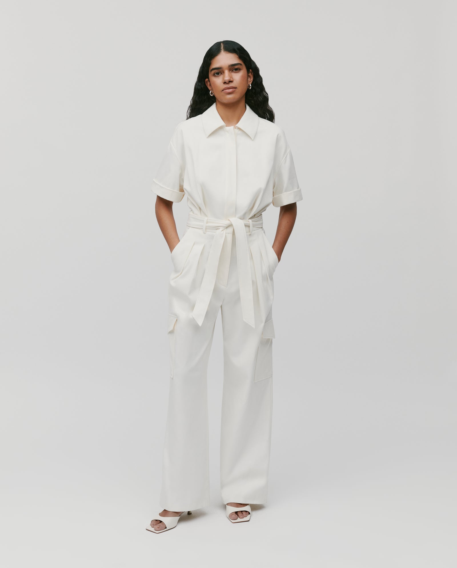 A model wears the IVY OAK PHILO Jumpsuit, featuring a fitted waist and barrel leg shape, styled with sandals and hands in pockets, against a plain background.