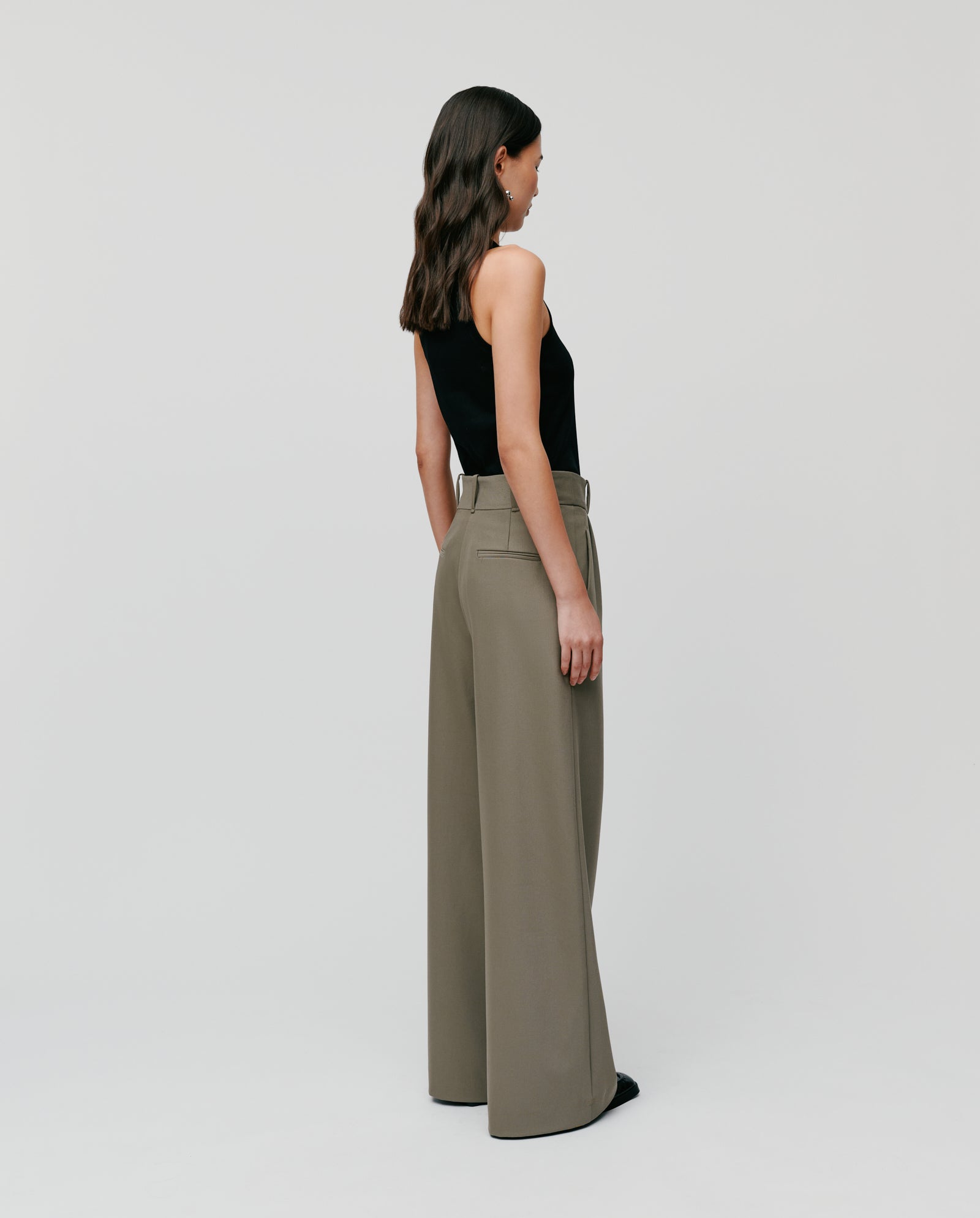 A woman in IVY OAK PRESCILLIA ANN high waist trousers with French pockets and a black sleeveless top stands against a plain background, viewed from behind.