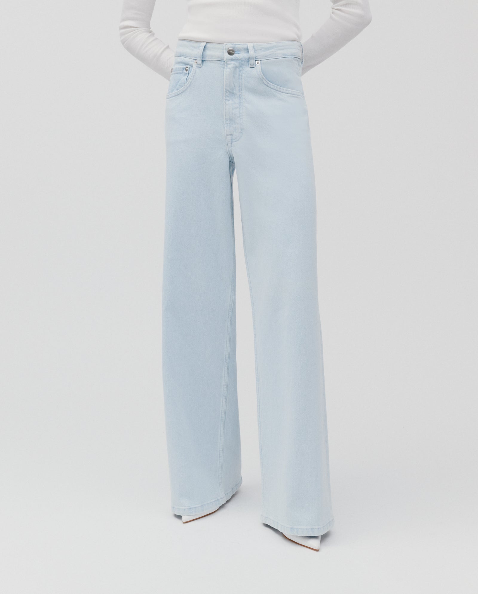 Model wearing IVY OAK PRIJANKA Jeans, featuring a high-waisted, wide-leg fit in a light wash, paired with a long-sleeve white top against a white background.