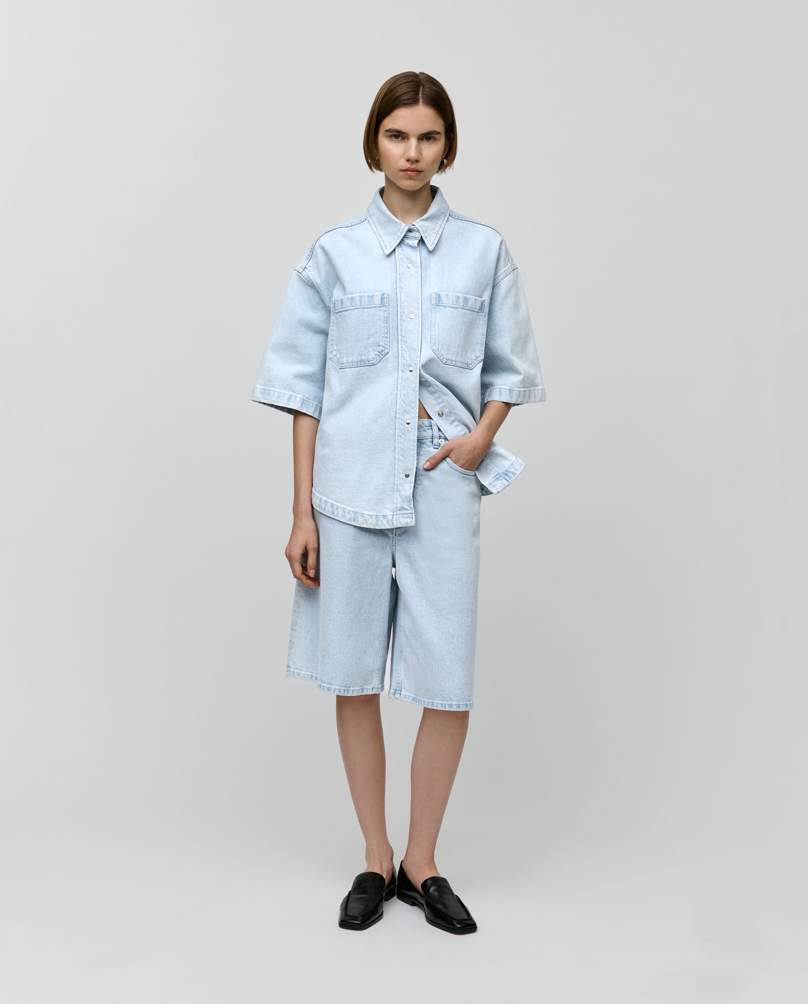 A woman in IVY OAK’s PIRI Pants and a light denim shirt stands against a plain background.