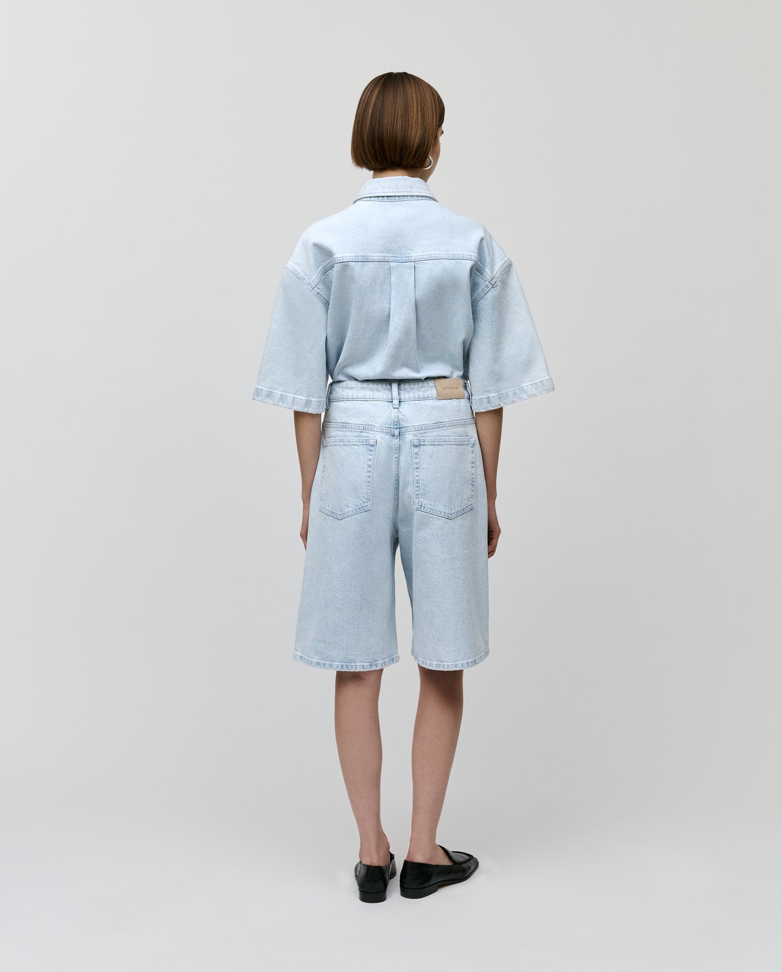 Model wearing IVY OAKs PIRI Pants, standing with back to camera, styled with a light denim shirt against a plain background.