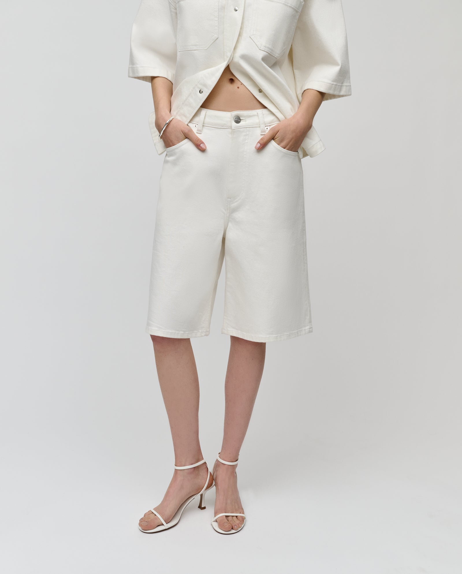 Woman wearing IVY OAK’s PIRI Pants styled with a white button-up shirt and white heeled sandals.