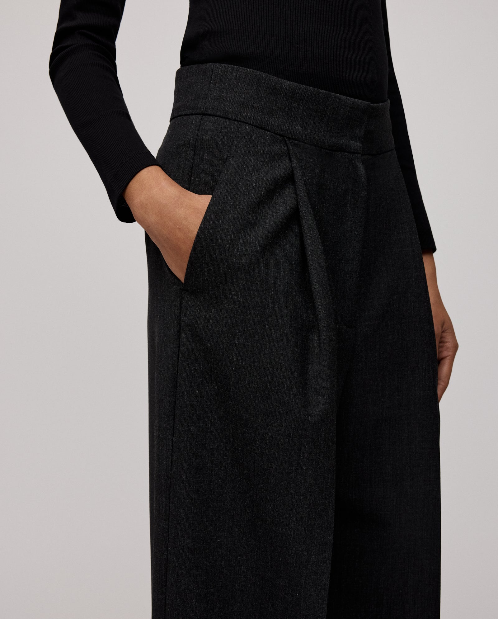 A person wears IVY OAK PRESCILLIA SUE wide leg pants and a black long-sleeve top, with one hand in their pocket.