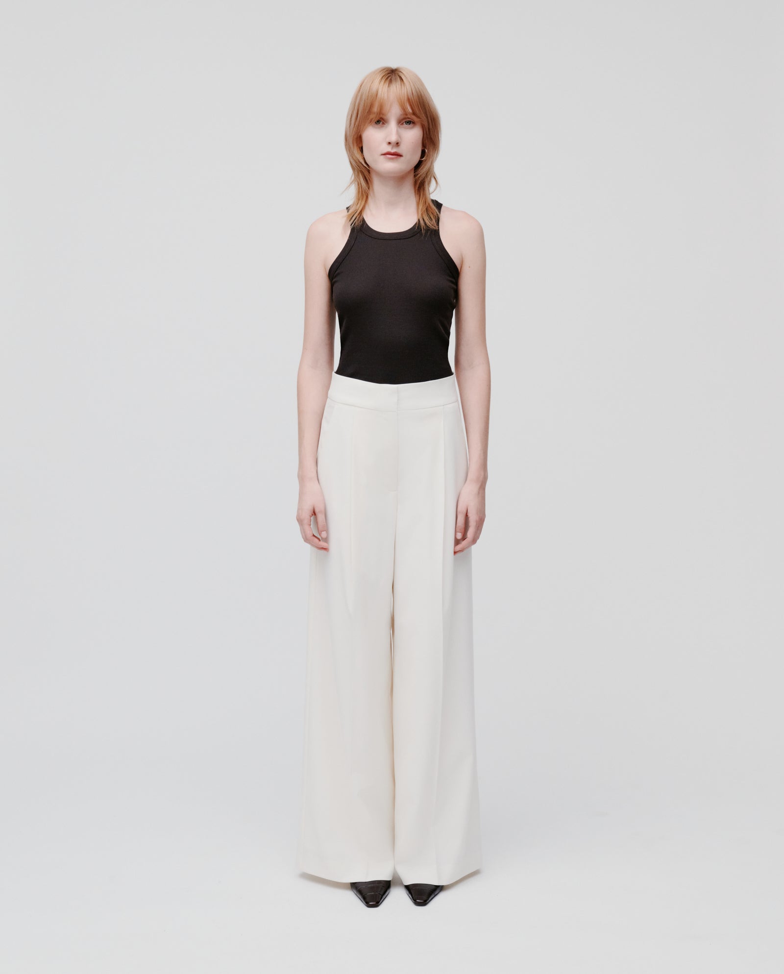 A woman in a black sleeveless top and IVY OAK’s PRESCILLIA SUE white wool-blend twill pants stands against a plain white background.