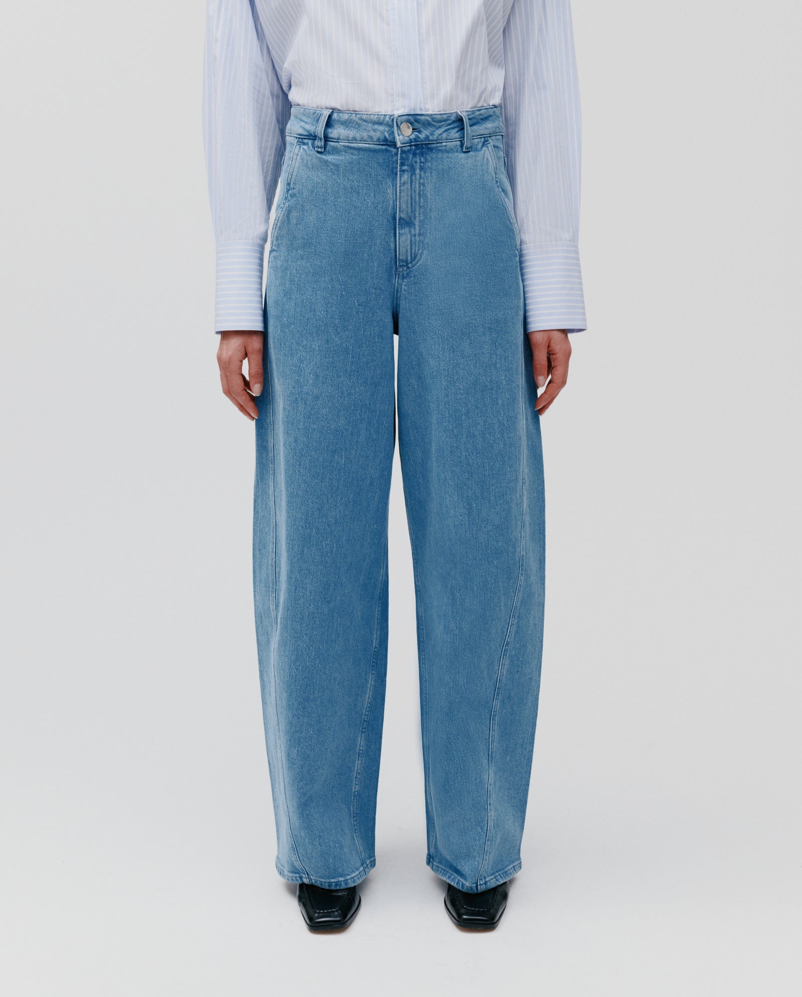 Model wears IVY OAKs PHILA Pants in blue denim with a white striped shirt, standing against a plain light background.