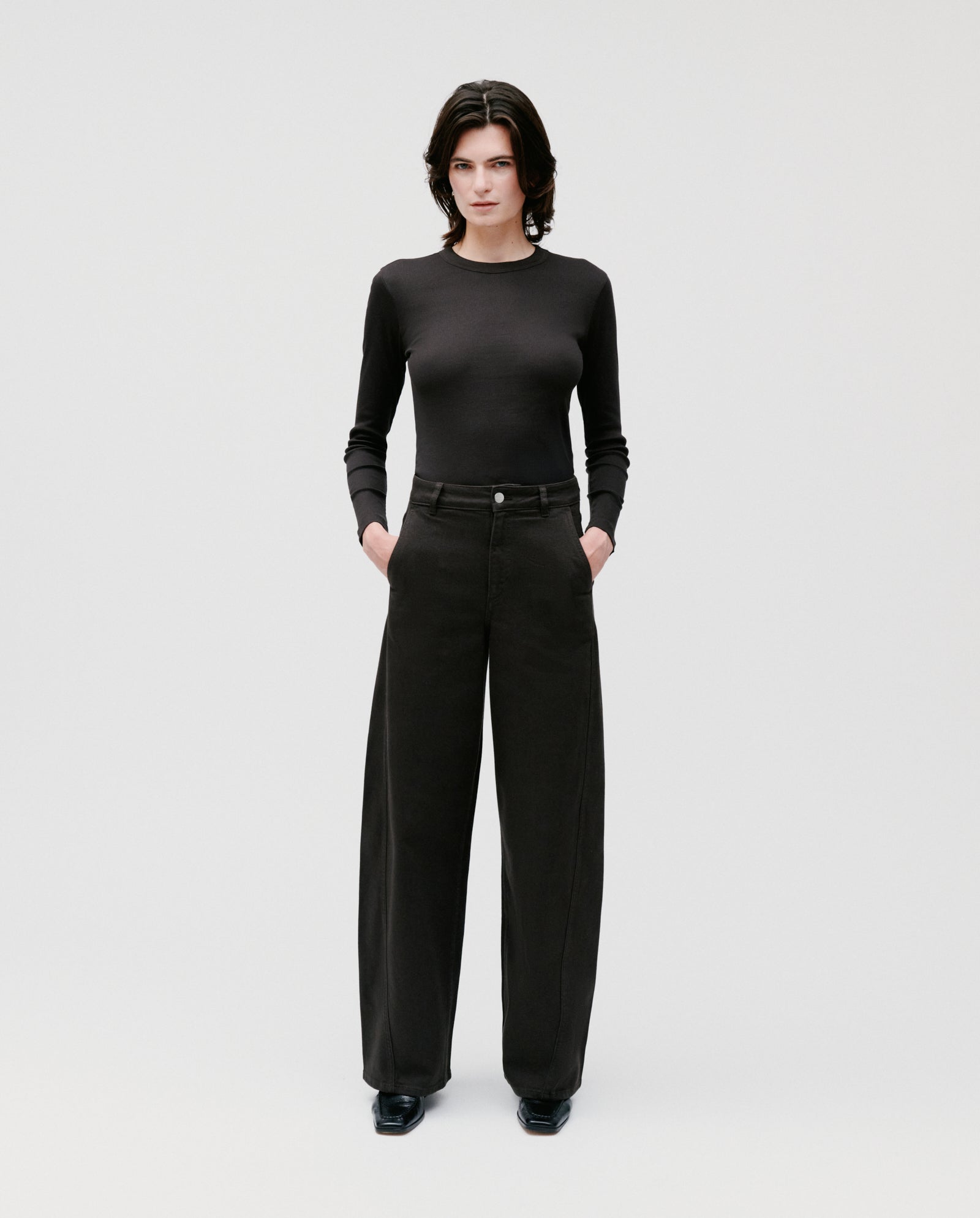 A person stands facing forward, wearing a black long-sleeve shirt and IVY OAKs PHILA Pants—deconstructed trousers with wide legs.