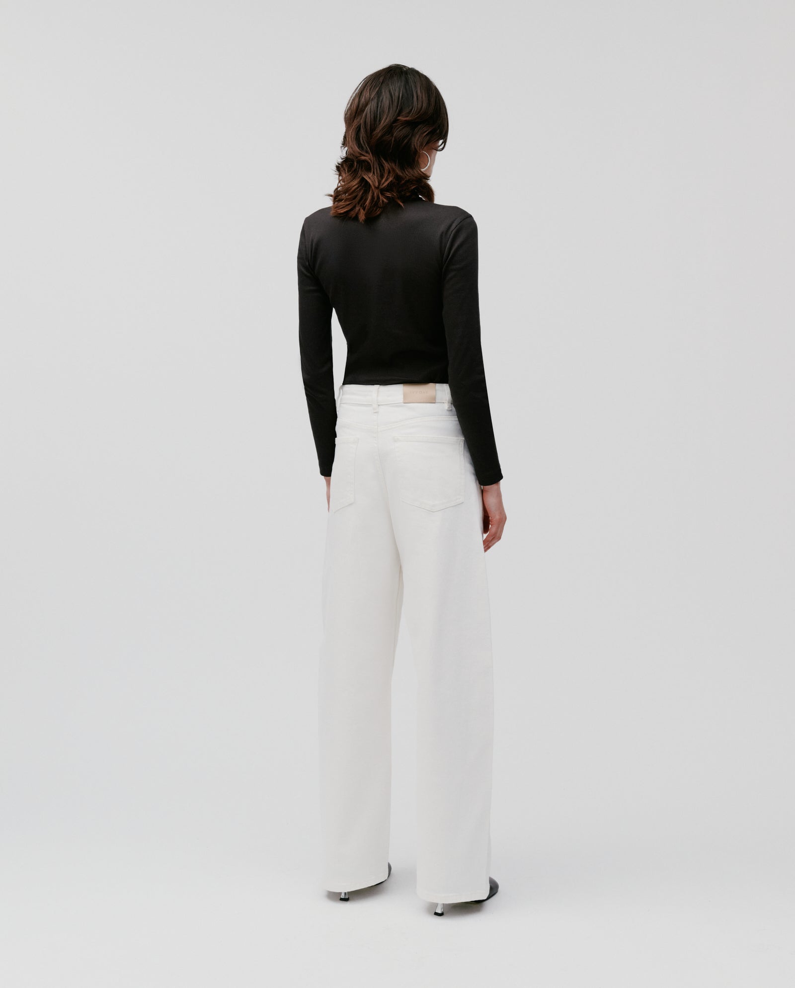 Person with shoulder-length hair, seen from behind, wearing a black long-sleeve top and IVY OAKs white PHILA Pants.