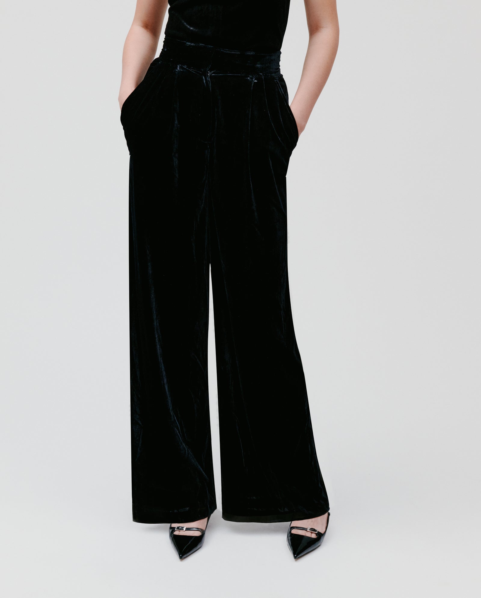 Model wears IVY OAK's PRESCILLIA ANN black women's velvet wide-leg pants with black pointed-toe heels, hands in pockets, against a plain background.