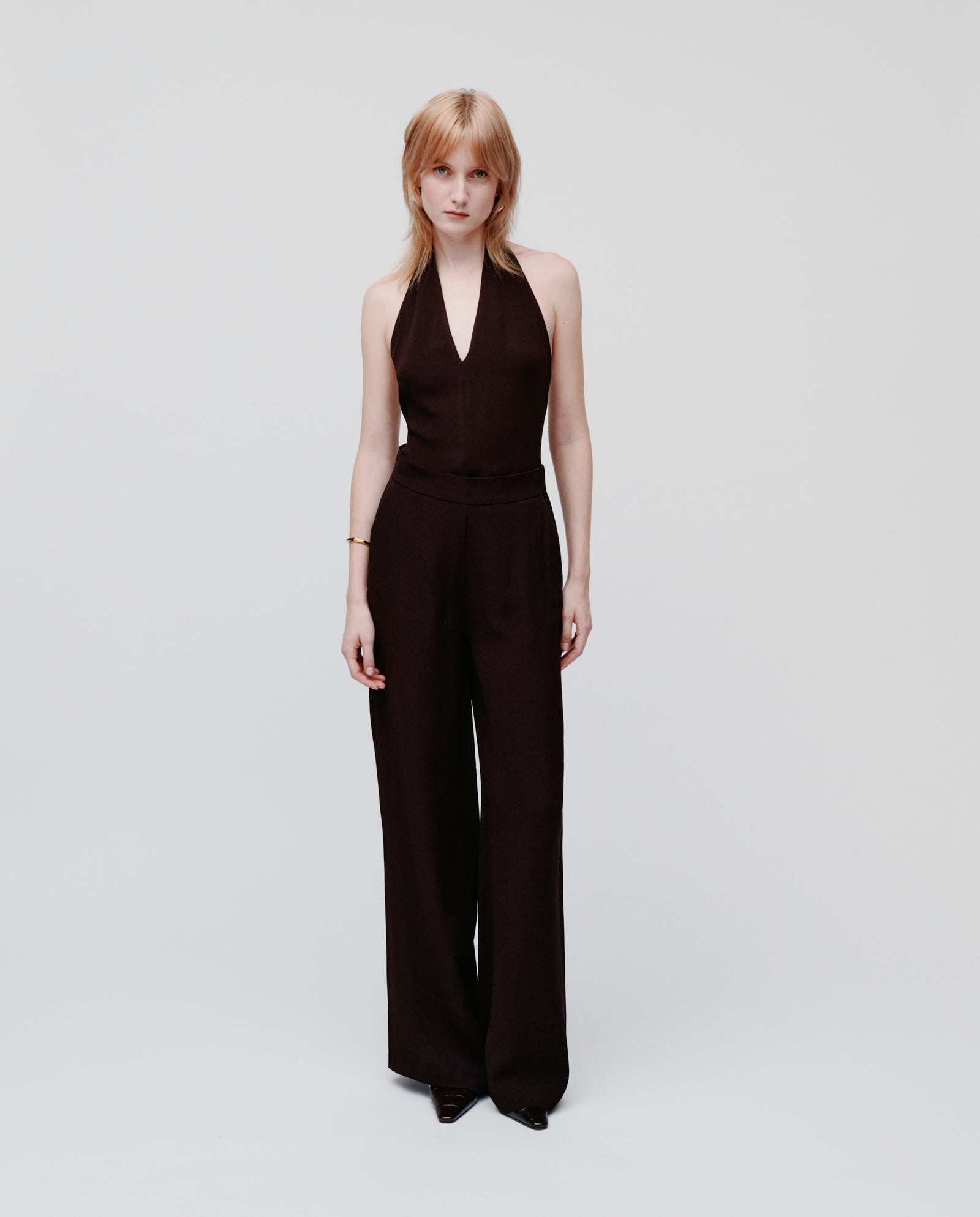 A woman stands against a plain white background wearing IVY OAKs PHILINE SUE Pants with black shoes and a sleeveless black halter top.