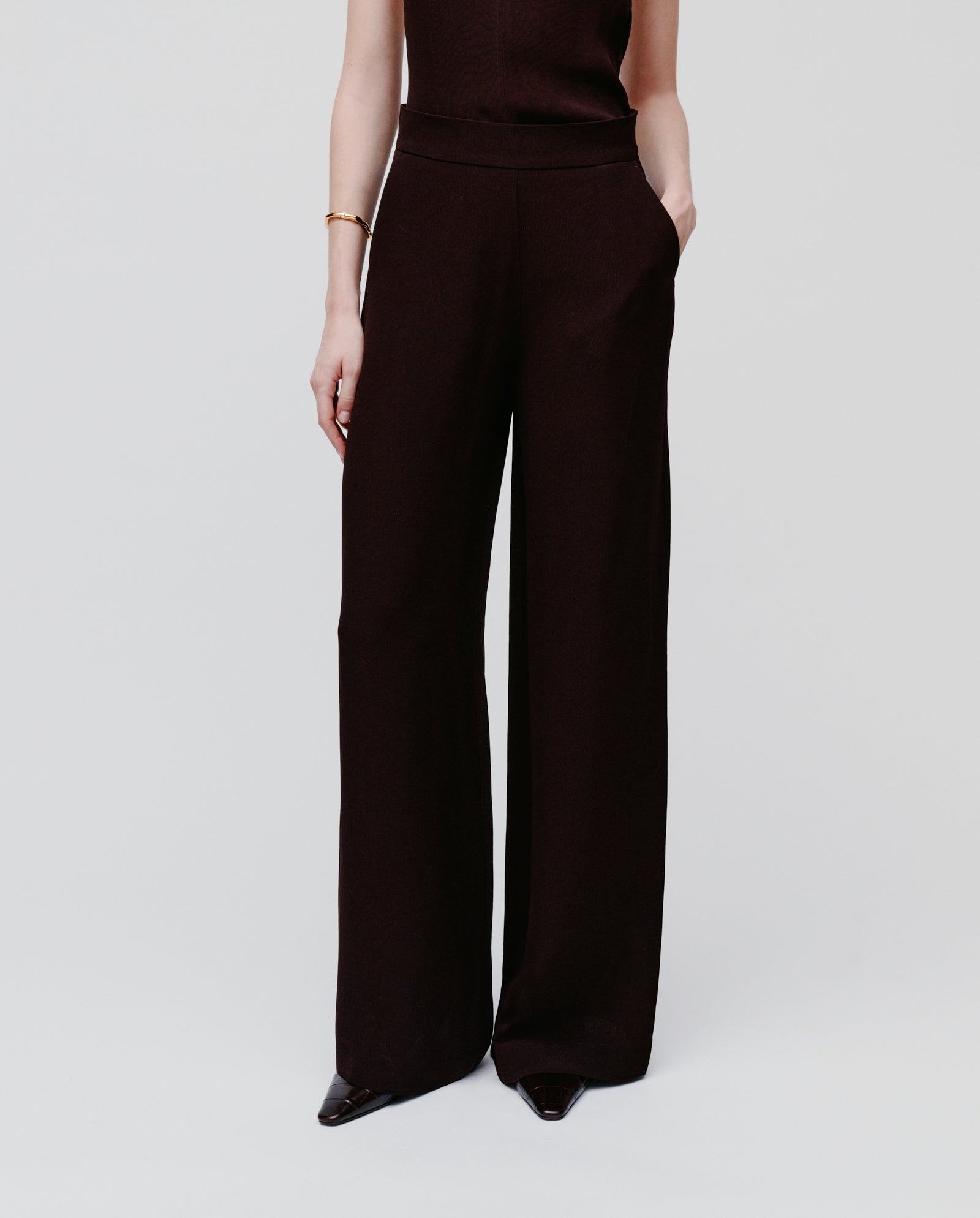 Model wears IVY OAK PHILINE SUE Pants, wide leg trousers in black crepe fabric, paired with a sleeveless top and one hand in pocket, standing against a plain background.