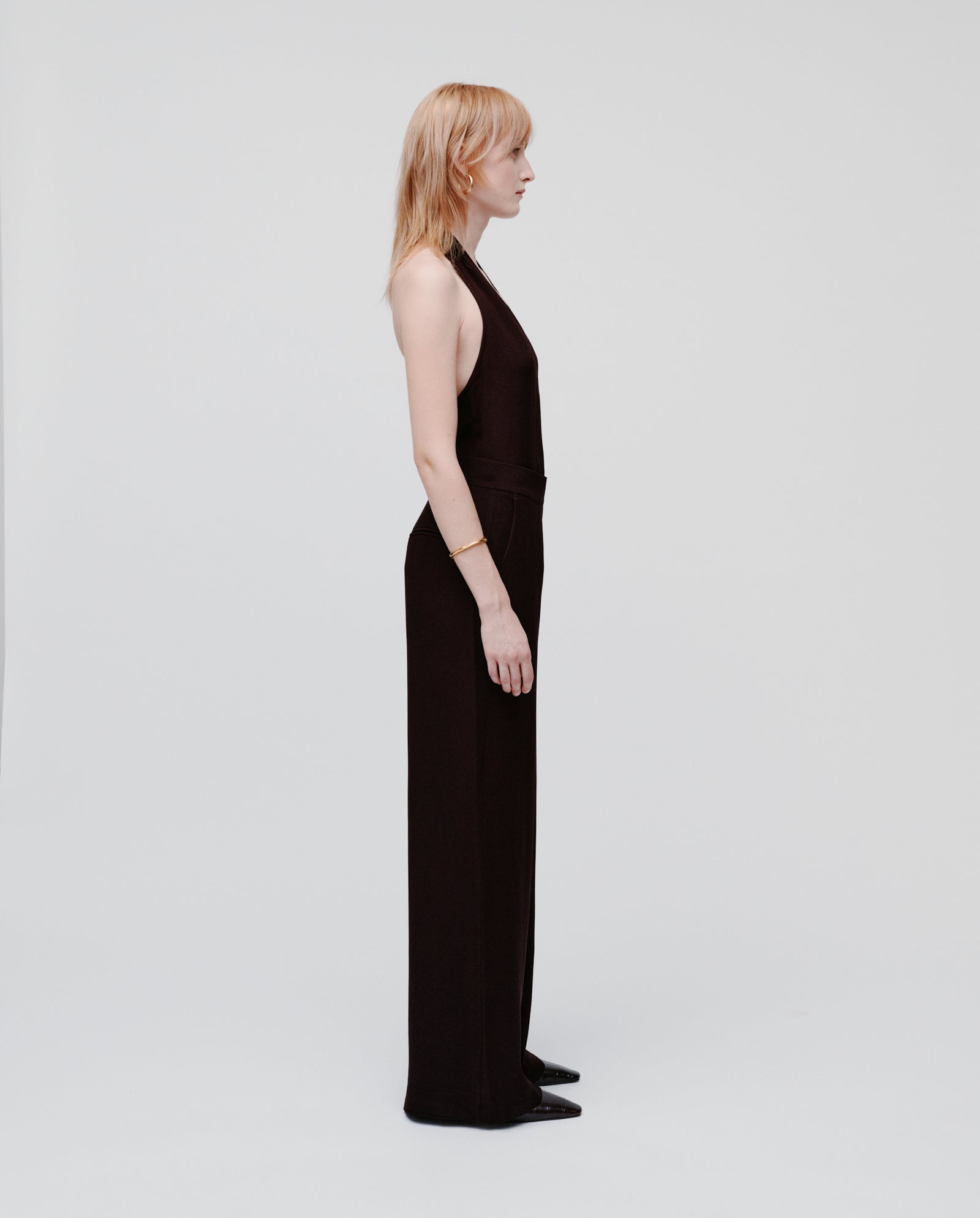 A woman with light hair wears IVY OAKs PHILINE SUE Pants, a black wide-leg jumpsuit, standing in profile against a plain white background.