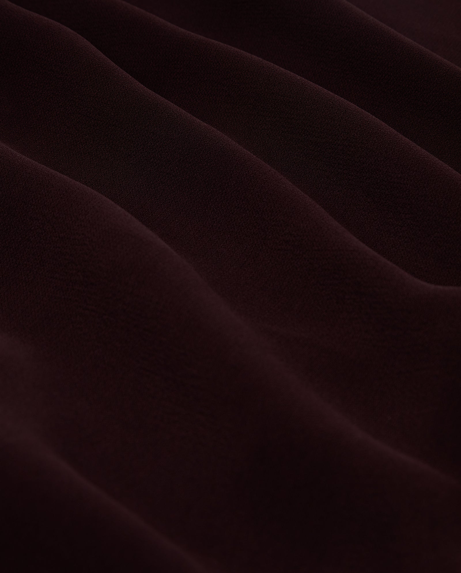 Close-up of PHILINE SUE Pants by IVY OAK, showcasing dark brown crepe fabric with soft, wavy folds and a subtly textured surface.