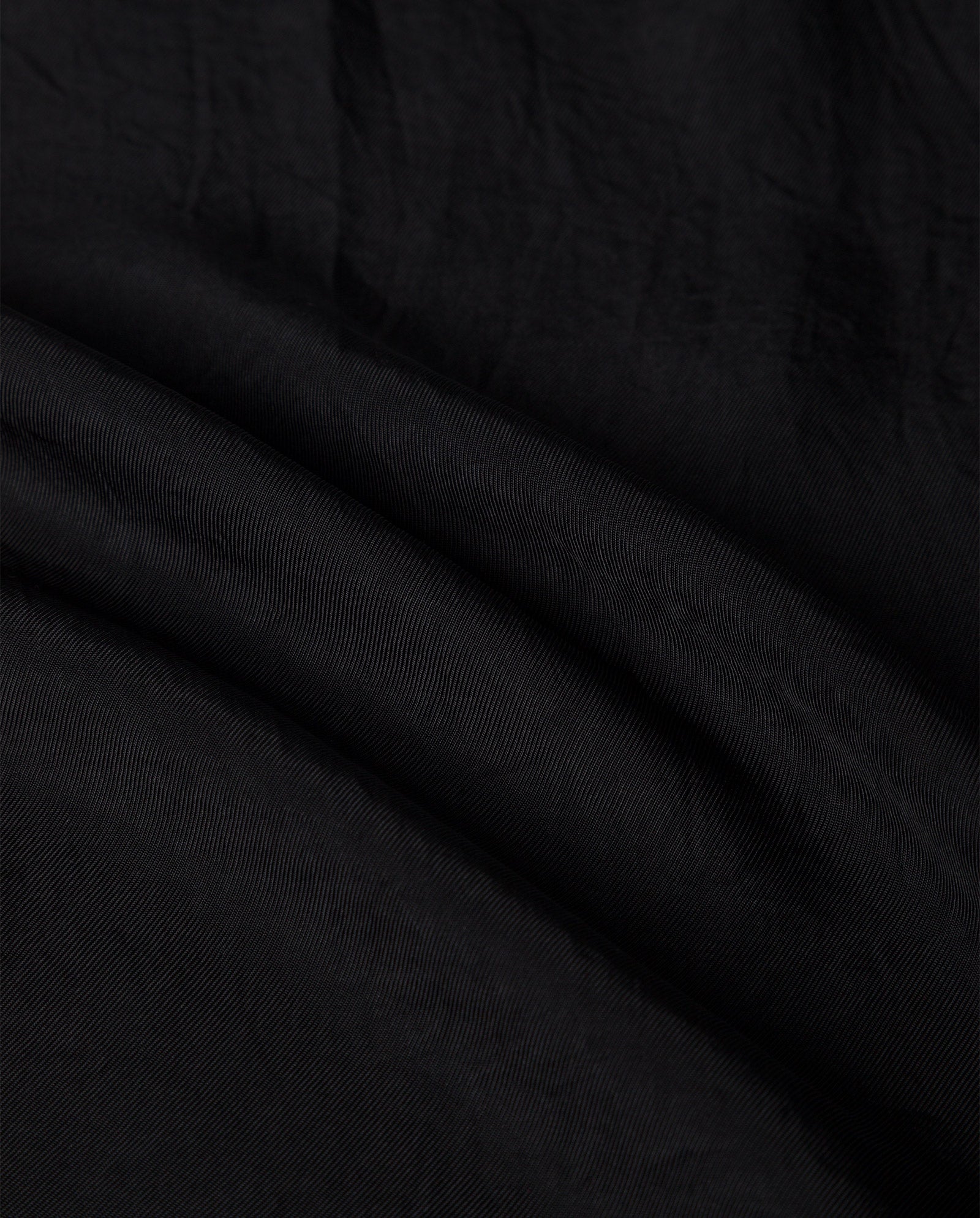 Close-up of the SYLVIA MAY Skirt by IVY OAK in black Naia acetate, showing its visible texture and gentle diagonal folds.