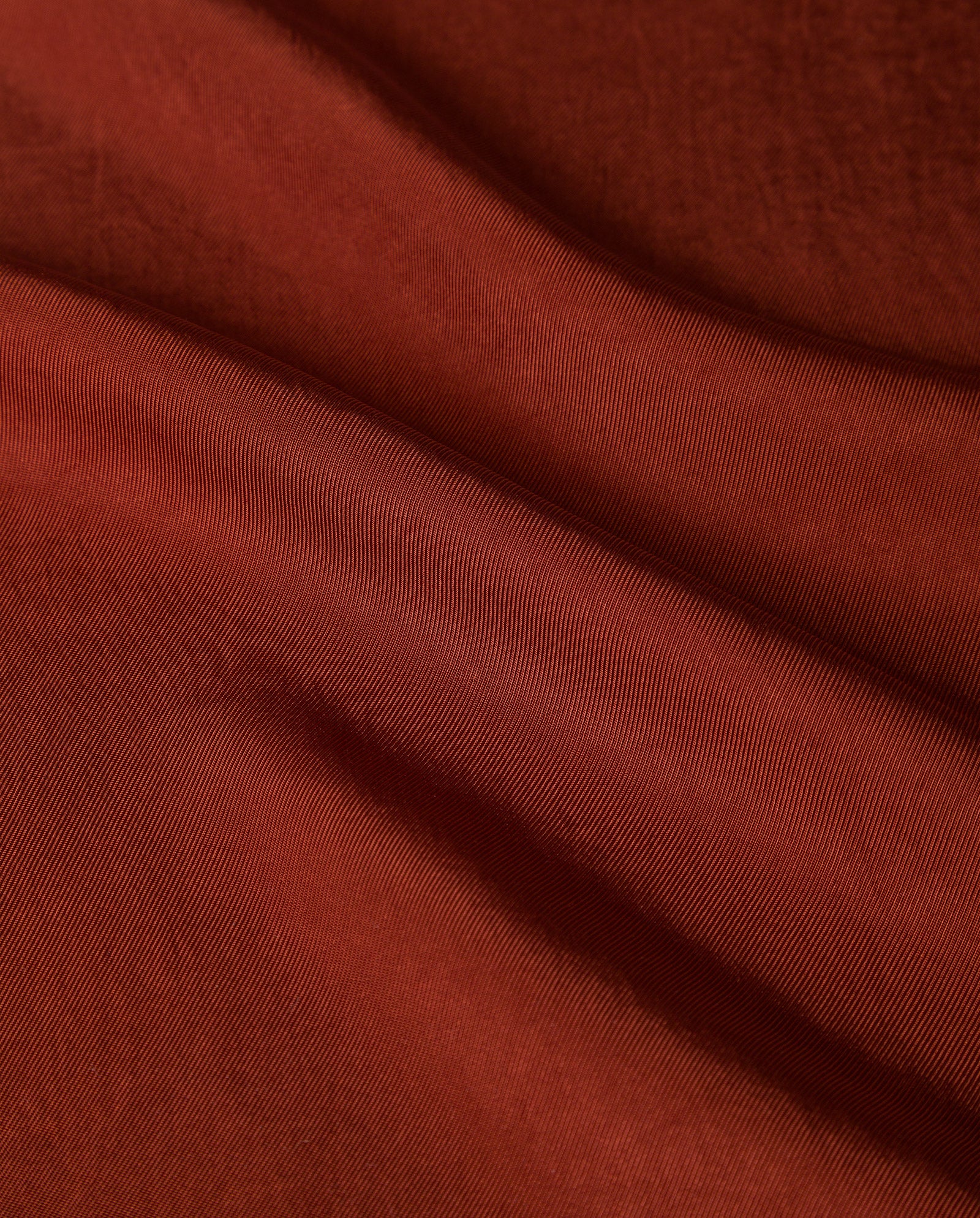 Close-up of the SYLVIA MAY Skirt by IVY OAK, crafted from smooth, reddish-brown Naia acetate fabric featuring gentle, flowing folds and a soft texture.