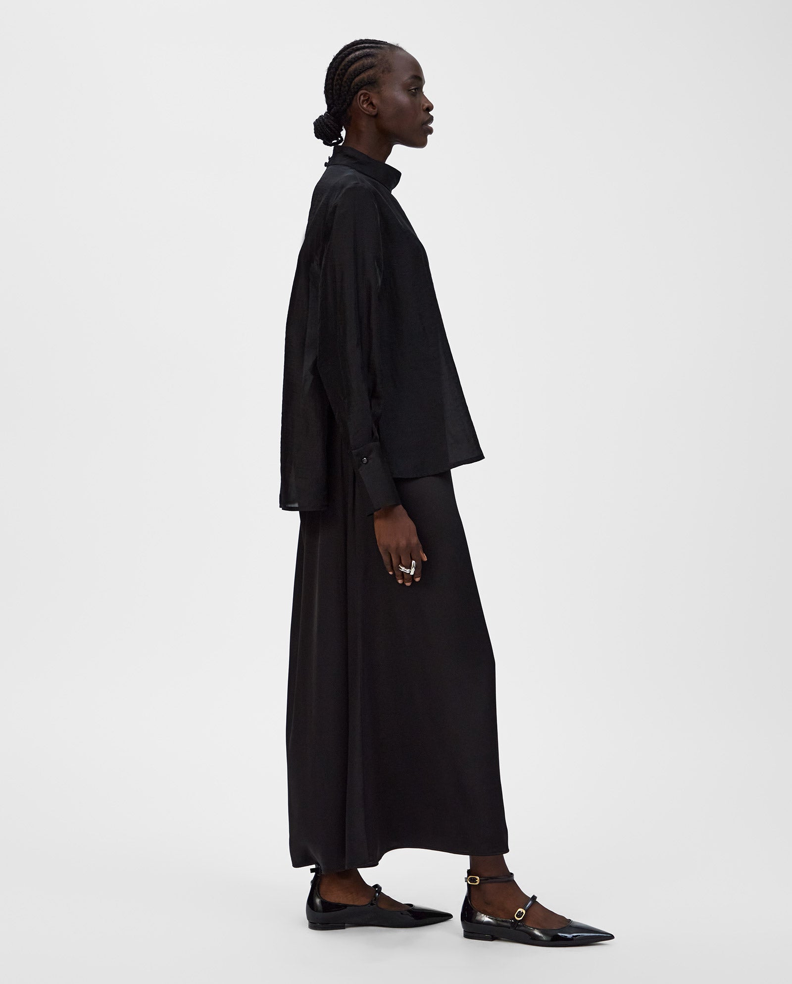 A woman in a black long-sleeve shirt and ankle-length IVY OAK SUMMER Skirt with black flats stands in profile against a white background.