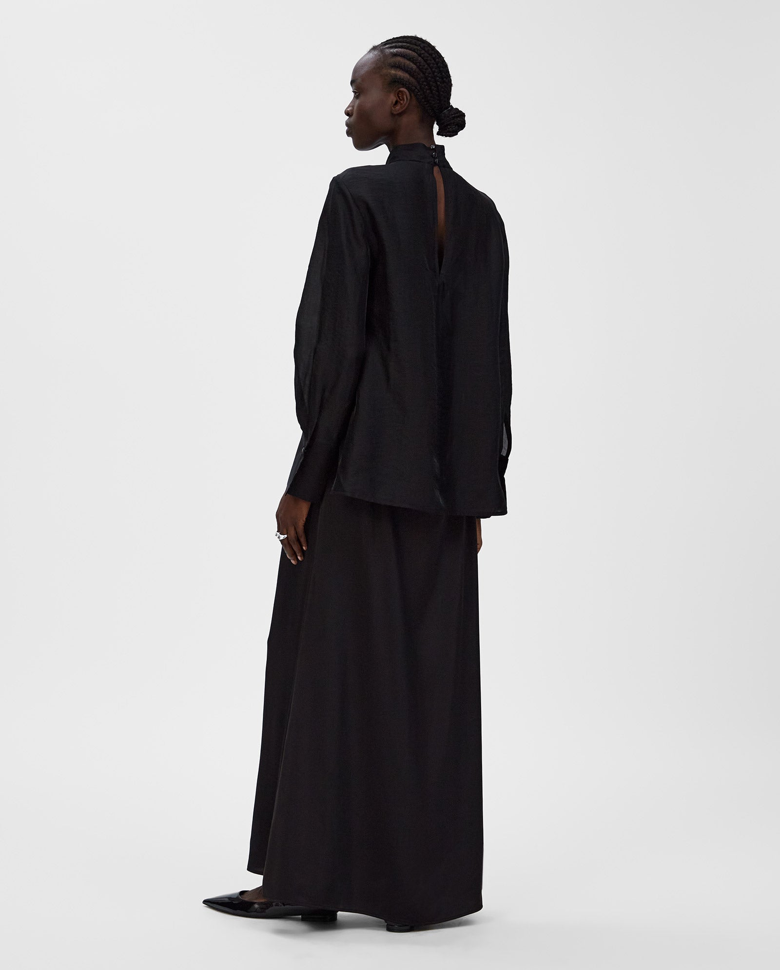 A woman in a loose black long-sleeve top and ankle-length IVY OAK SUMMER Skirt stands sideways against a plain white background.