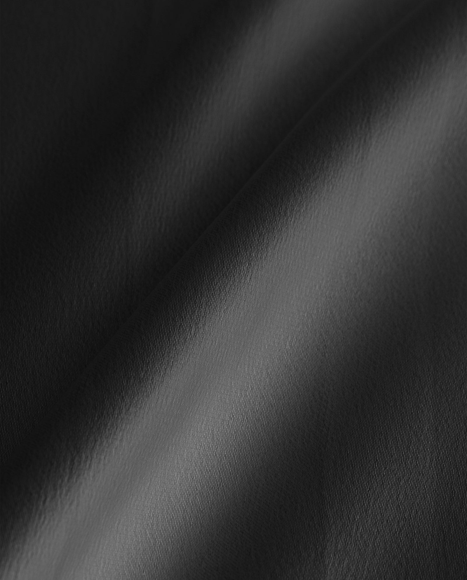 Close-up of smooth, black satin fabric with soft light and gentle folds, recalling the effortless elegance of IVY OAKs ankle-length SUMMER Skirt.