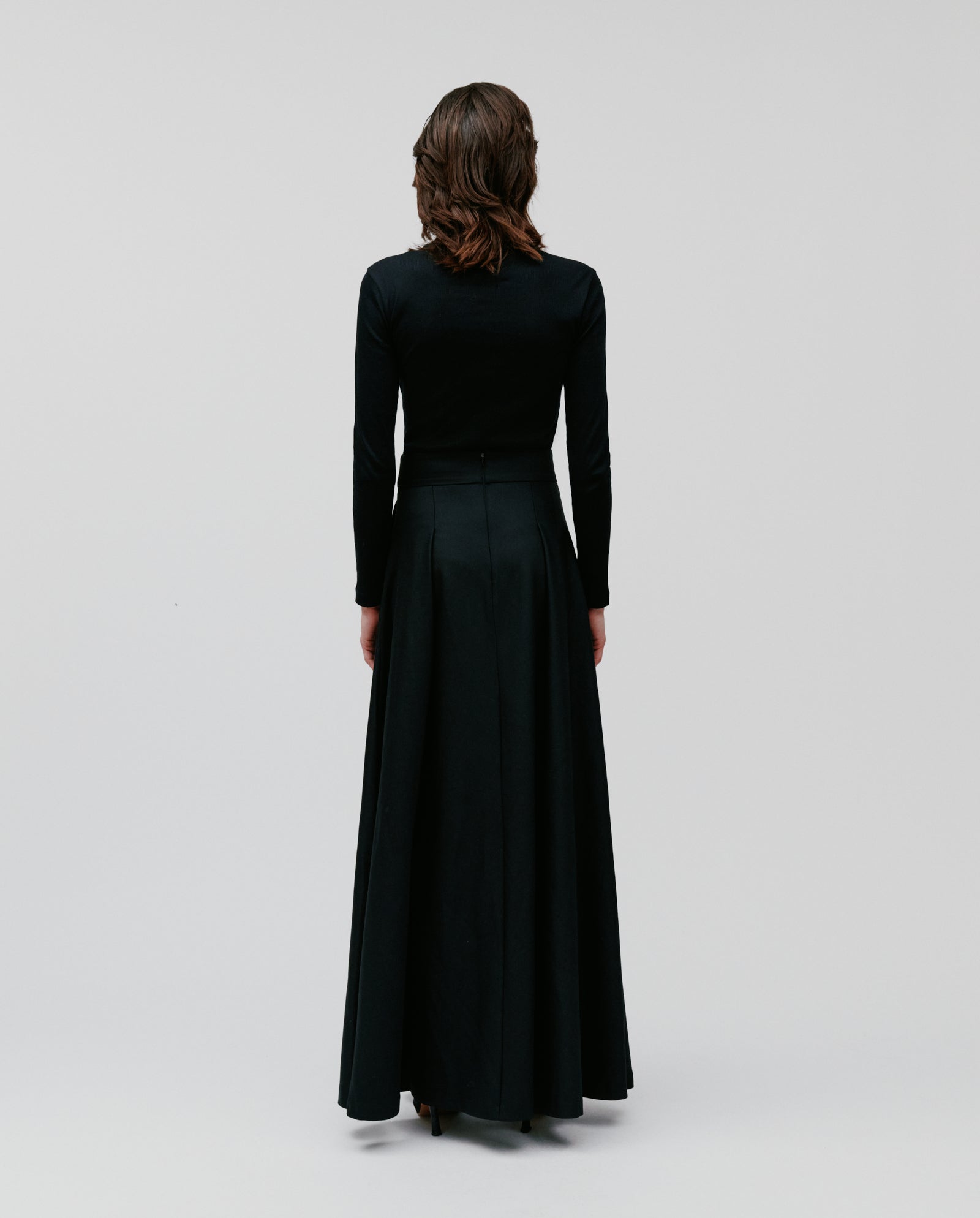 A person with wavy brown hair, shown from behind, wears the IVY OAK SUSANNA black maxi-length skirt with pockets.