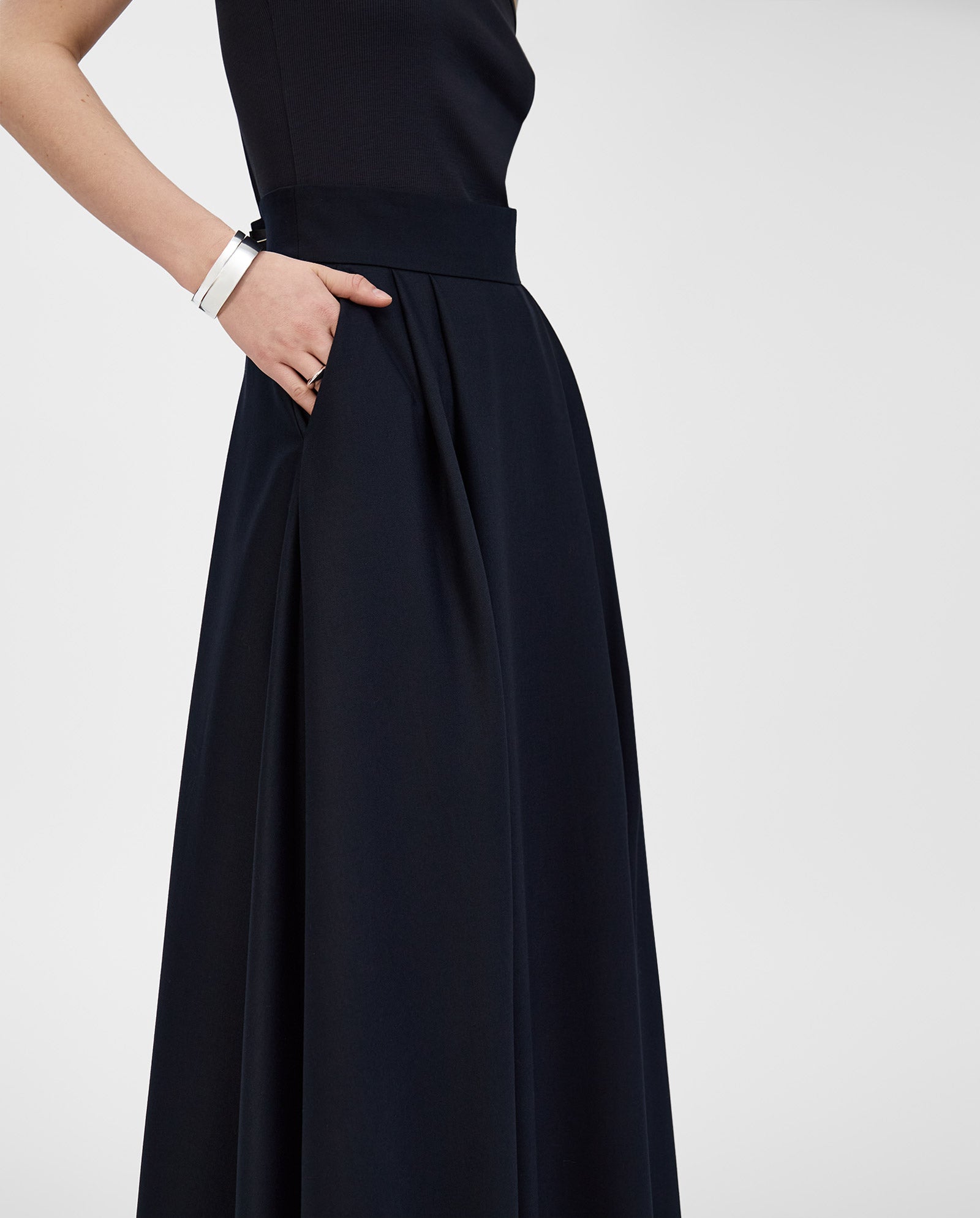 A woman in a sleeveless black dress with her hand in the pocket, seen from the side against a plain background, pairs it effortlessly with the IVY OAK SUSANNA Skirt for added voluminous flair.