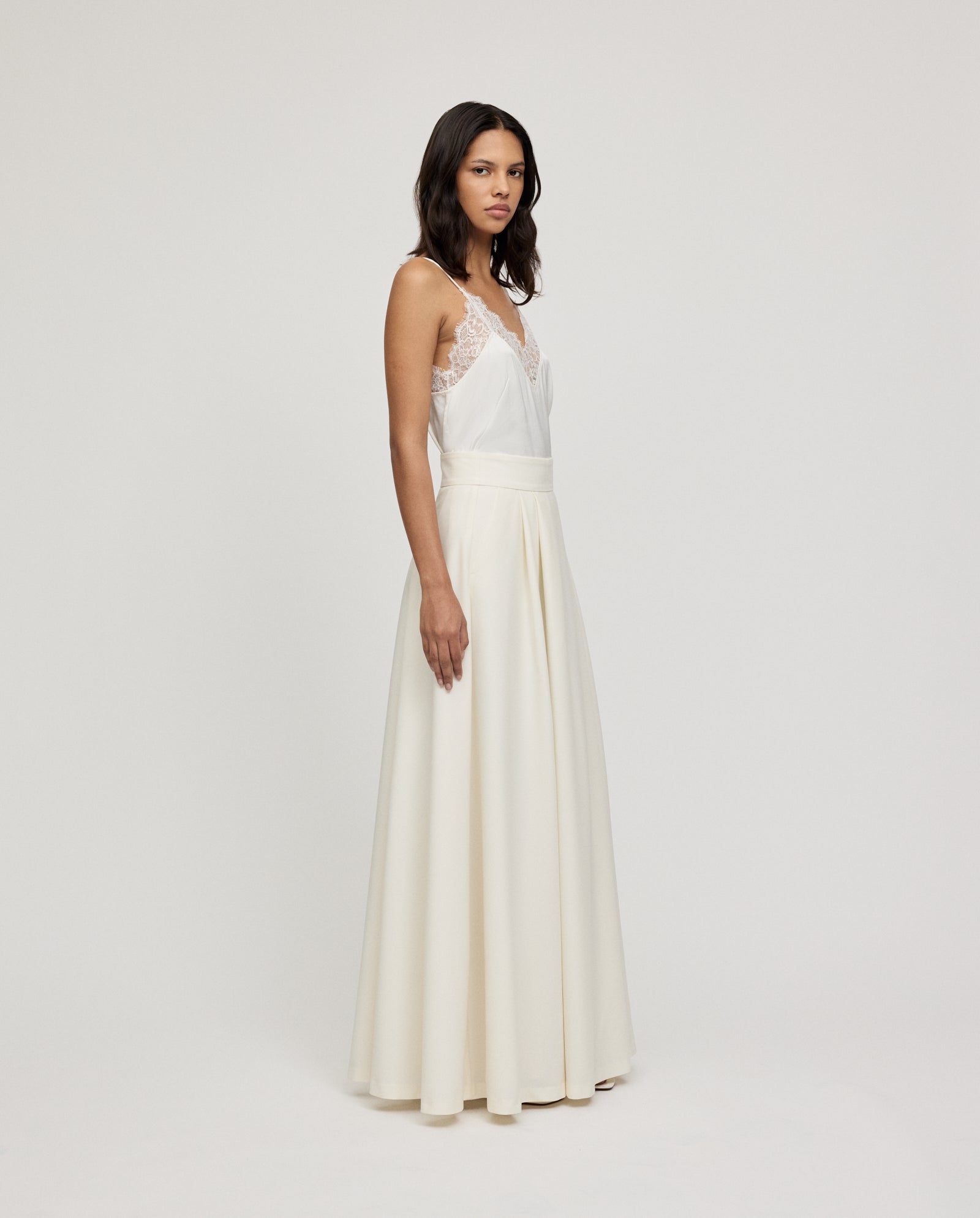 A woman models the IVY OAK SUSANNA Skirt, a maxi-length white skirt with lace detailing, set against a plain light background.