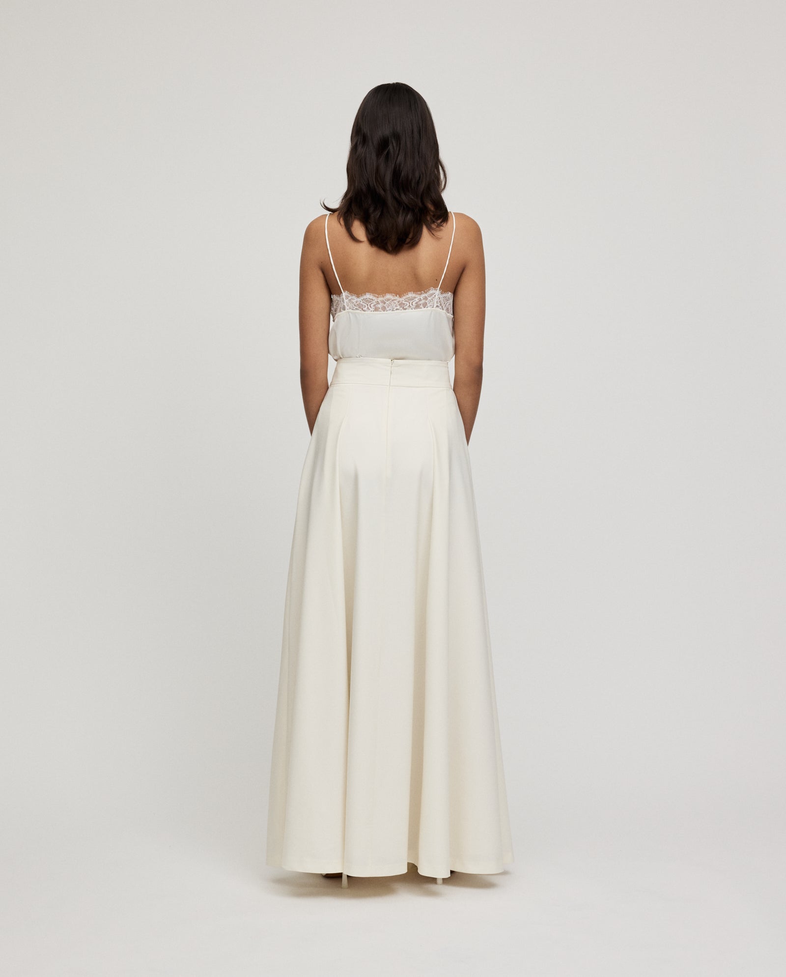 A woman stands with her back to the camera, wearing a white sleeveless lace top and an IVY OAK SUSANNA Skirt in maxi length.