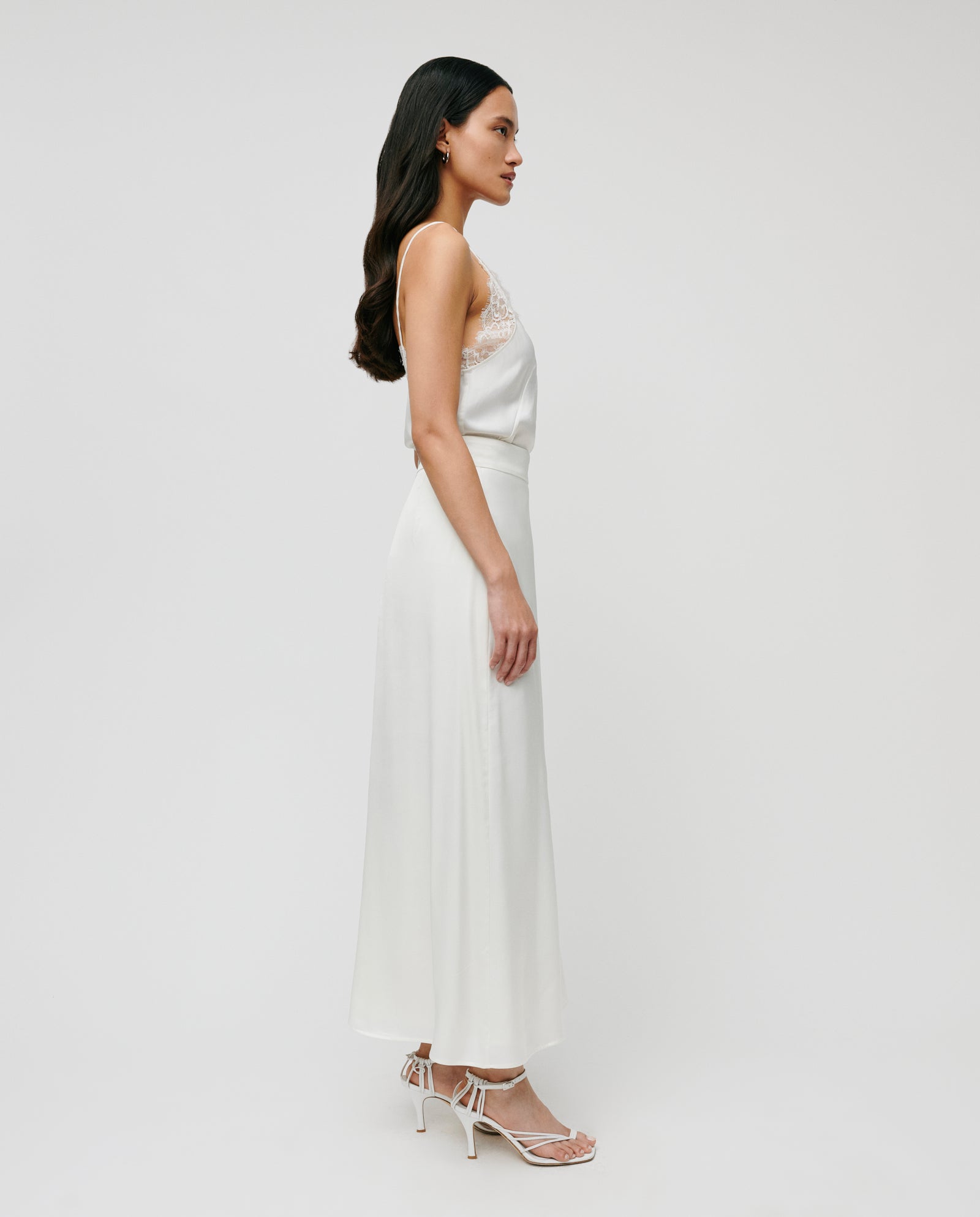 A woman in a white sleeveless top and the IVY OAK SANNA Skirt with heels stands in profile against a plain white background.